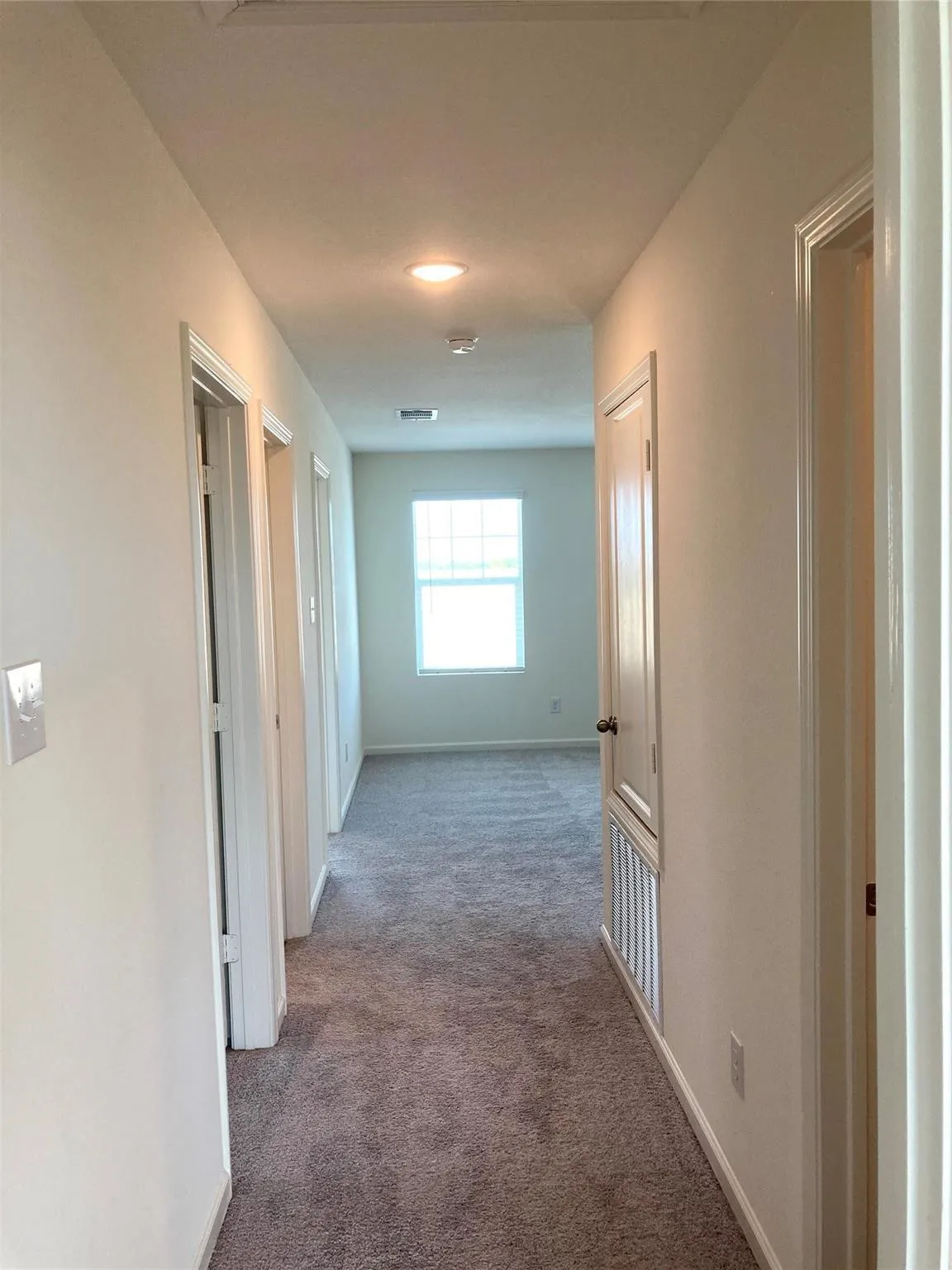 Carpeted hallway with white walls and multiple doorways