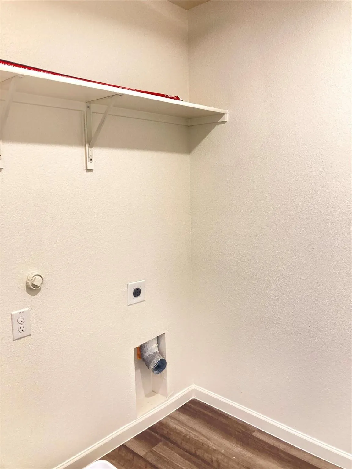 Dedicated laundry space featuring wood-finish flooring, white walls, and a built-in white shelf