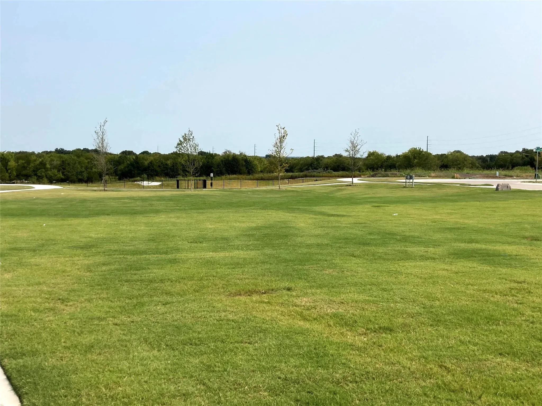 Expansive green space featuring a manicured lawn, established trees, and a pond with surrounding foliage