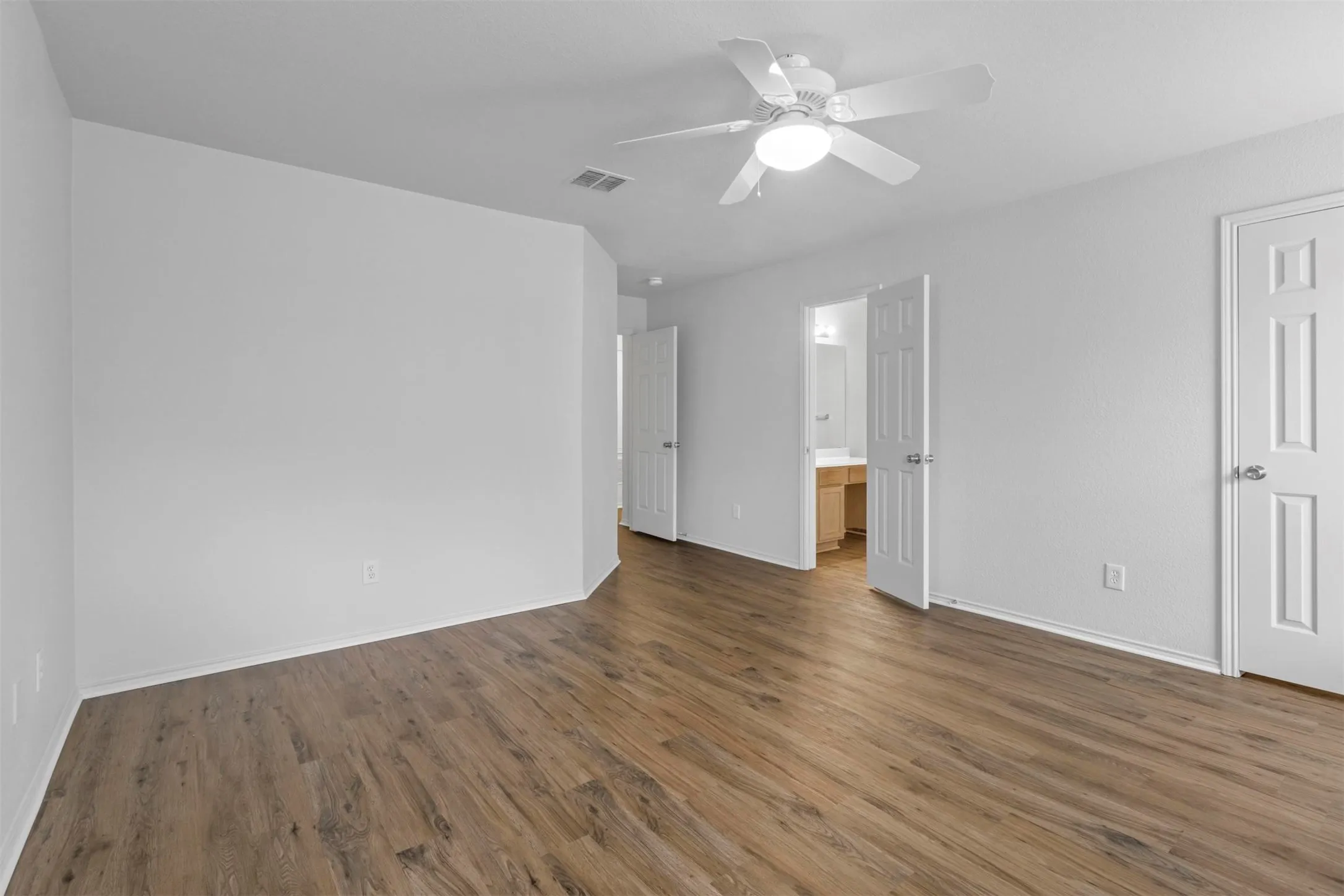 Spacious interior featuring wood-finish flooring, crisp white walls, and a ceiling fan with integrated lighting