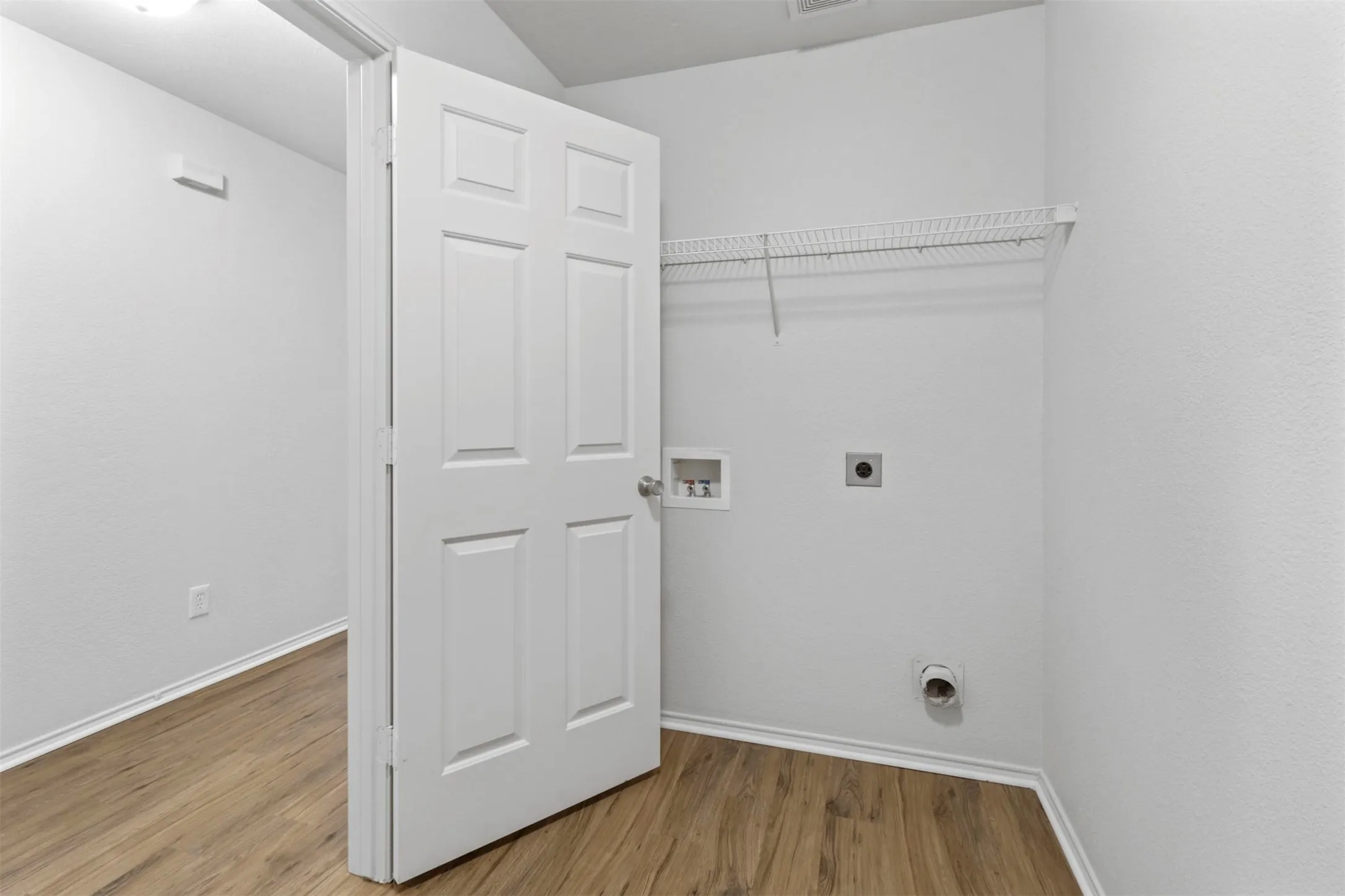 Utility area featuring wood-finish flooring, white walls, and a wire shelf