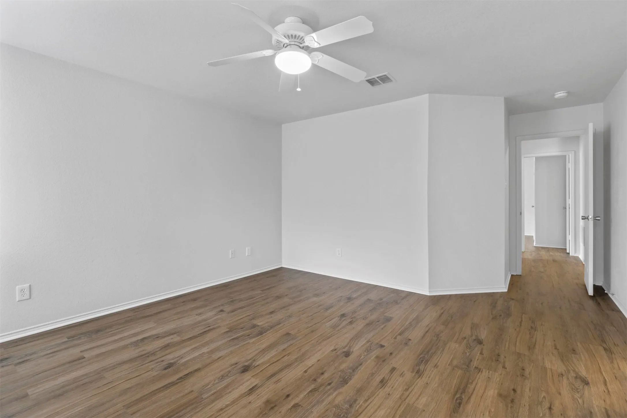 Spacious interior room featuring wood-finish flooring, crisp white walls, and a ceiling fan with integrated lighting