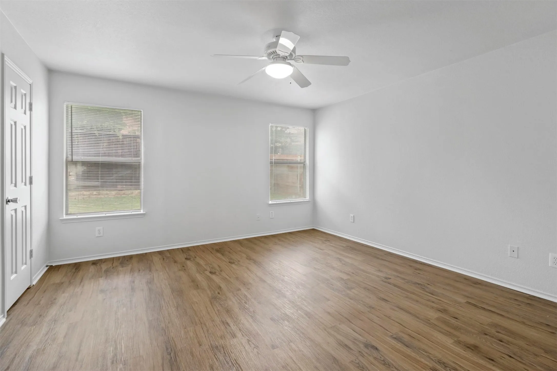 Spacious room showcasing gleaming wood-finish flooring, white walls, and abundant natural light from two large windows