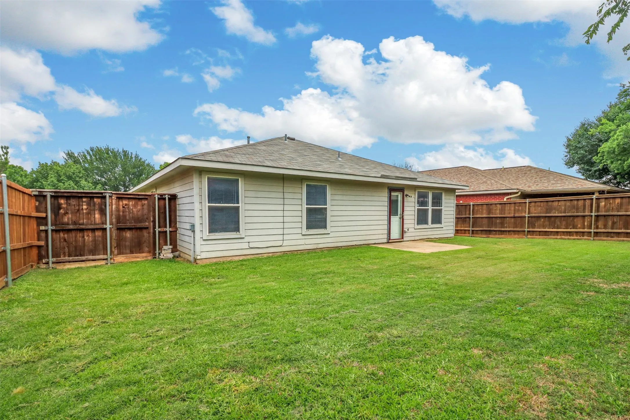 Expansive backyard featuring a lush lawn, privacy fencing, and a concrete patio