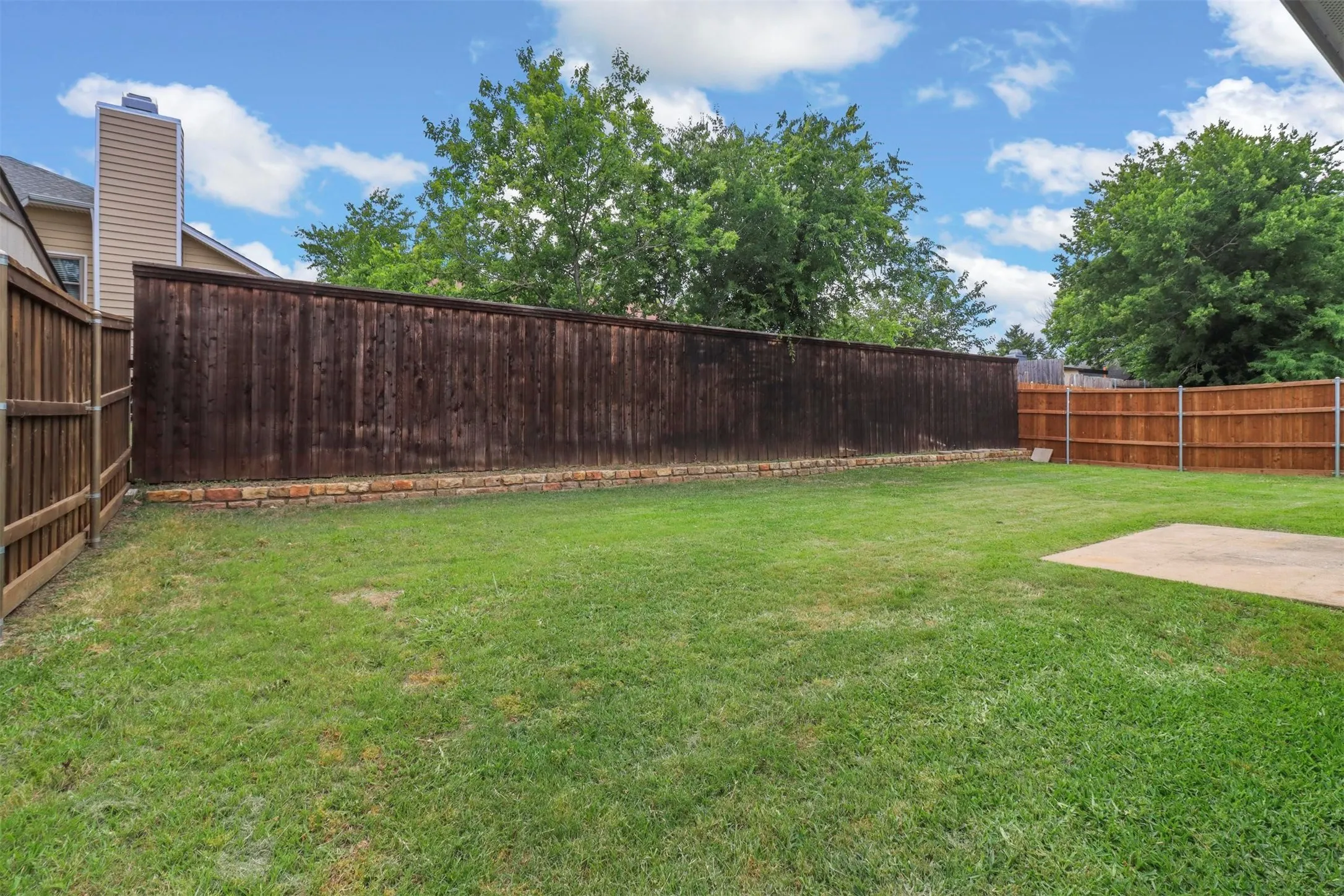 Expansive grassy yard with a concrete patio pad, bordered by tall privacy fencing