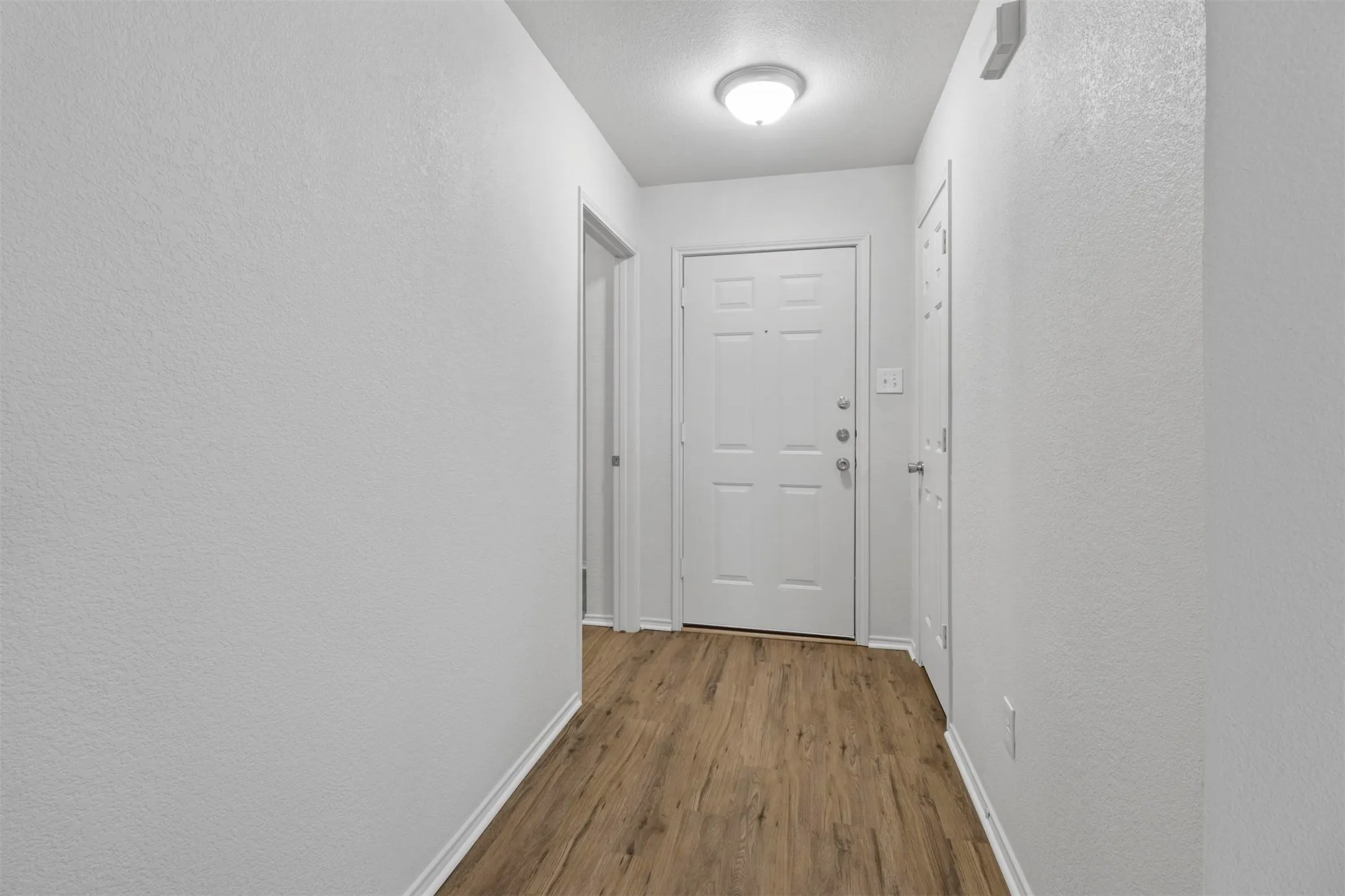 Entryway featuring a six-panel door, wood-finish flooring, white baseboards, textured walls, and a flush-mount ceiling light