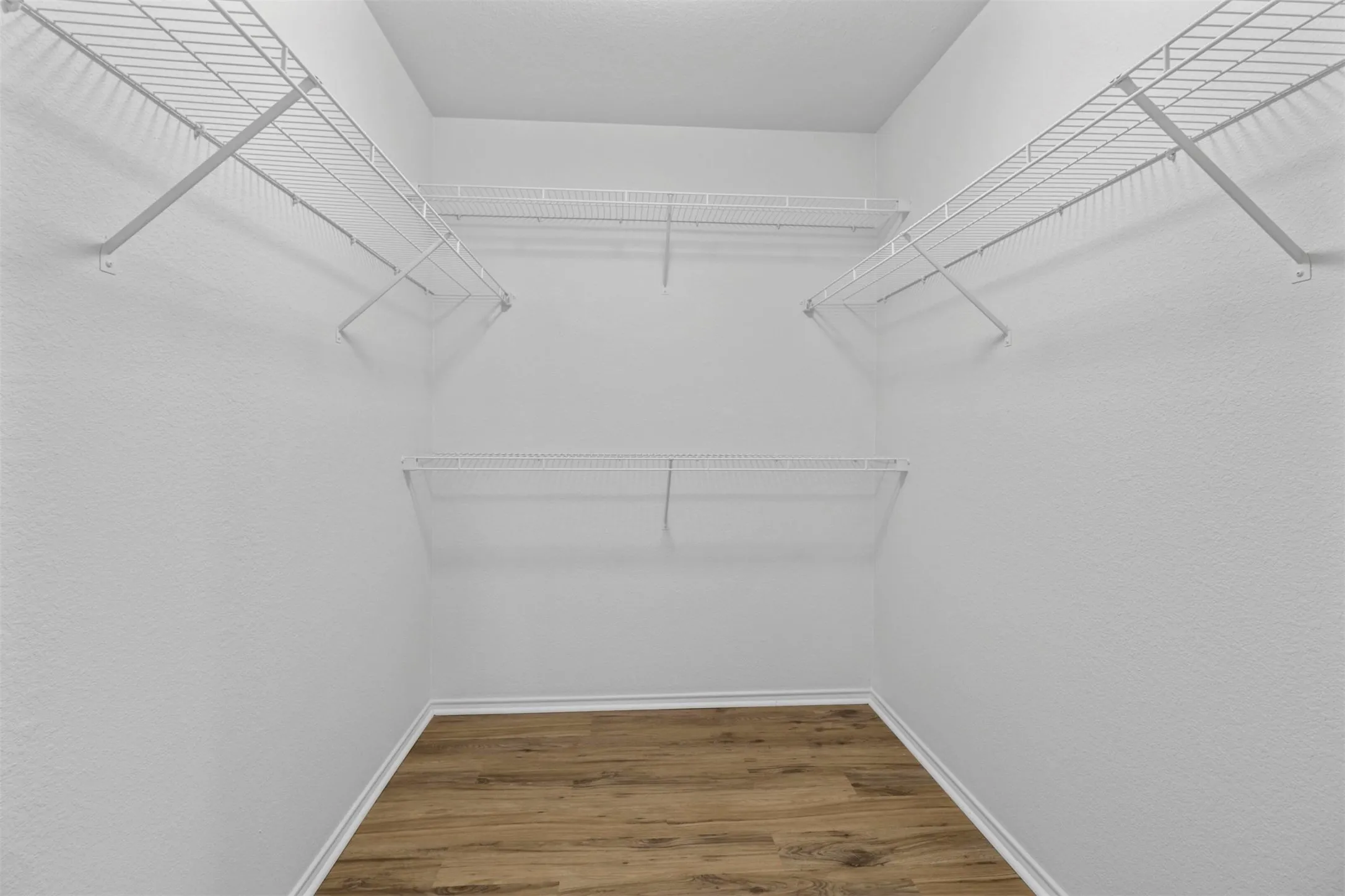 Walk-in closet featuring wood-finish flooring, white baseboards, and multiple tiers of white wire shelving