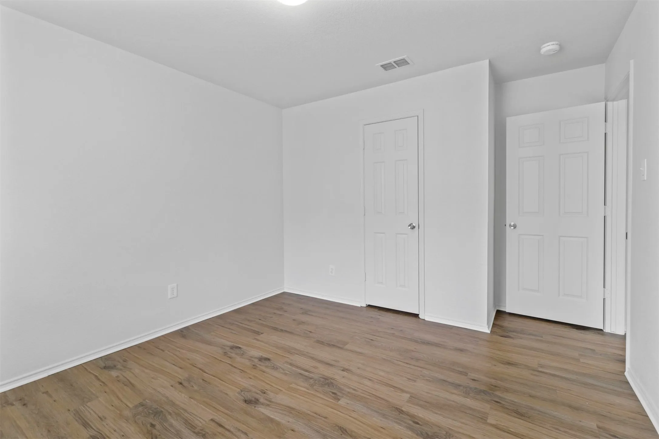 Room with wood-finish flooring, white baseboards, and white walls