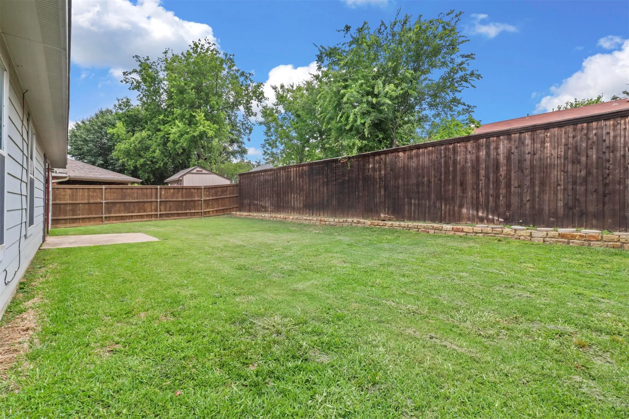 Spacious backyard featuring a manicured lawn, a concrete patio area, and perimeter fencing