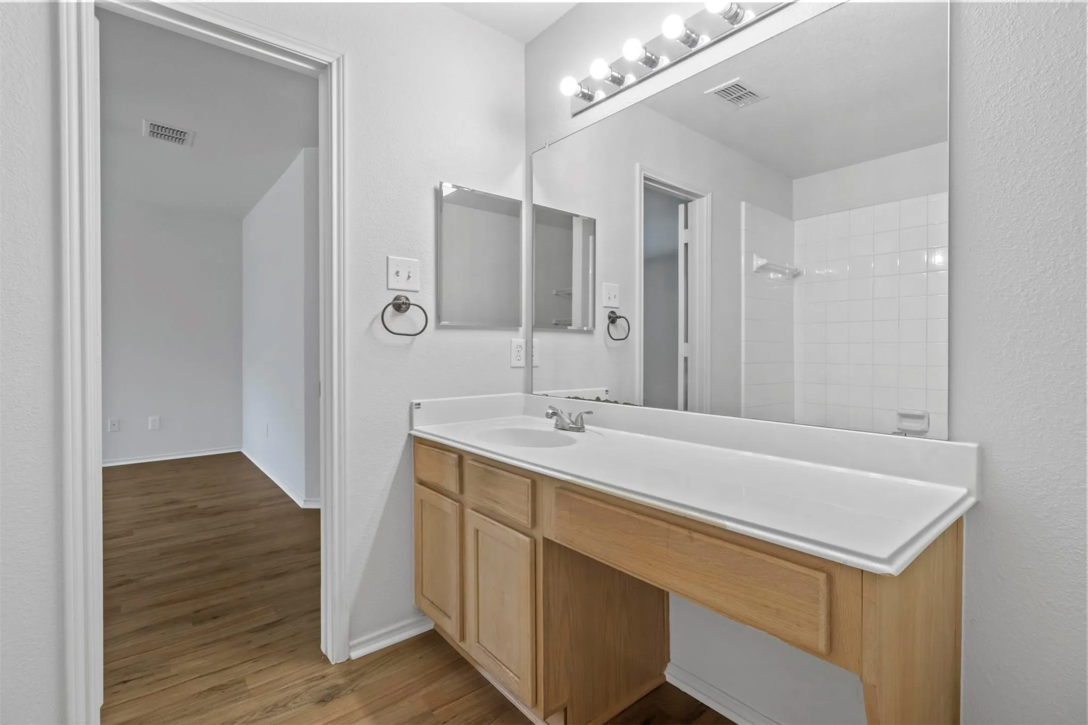 Bathroom featuring a light wood-finish vanity with an integrated sink, a white countertop, and a large wall-mounted mirror