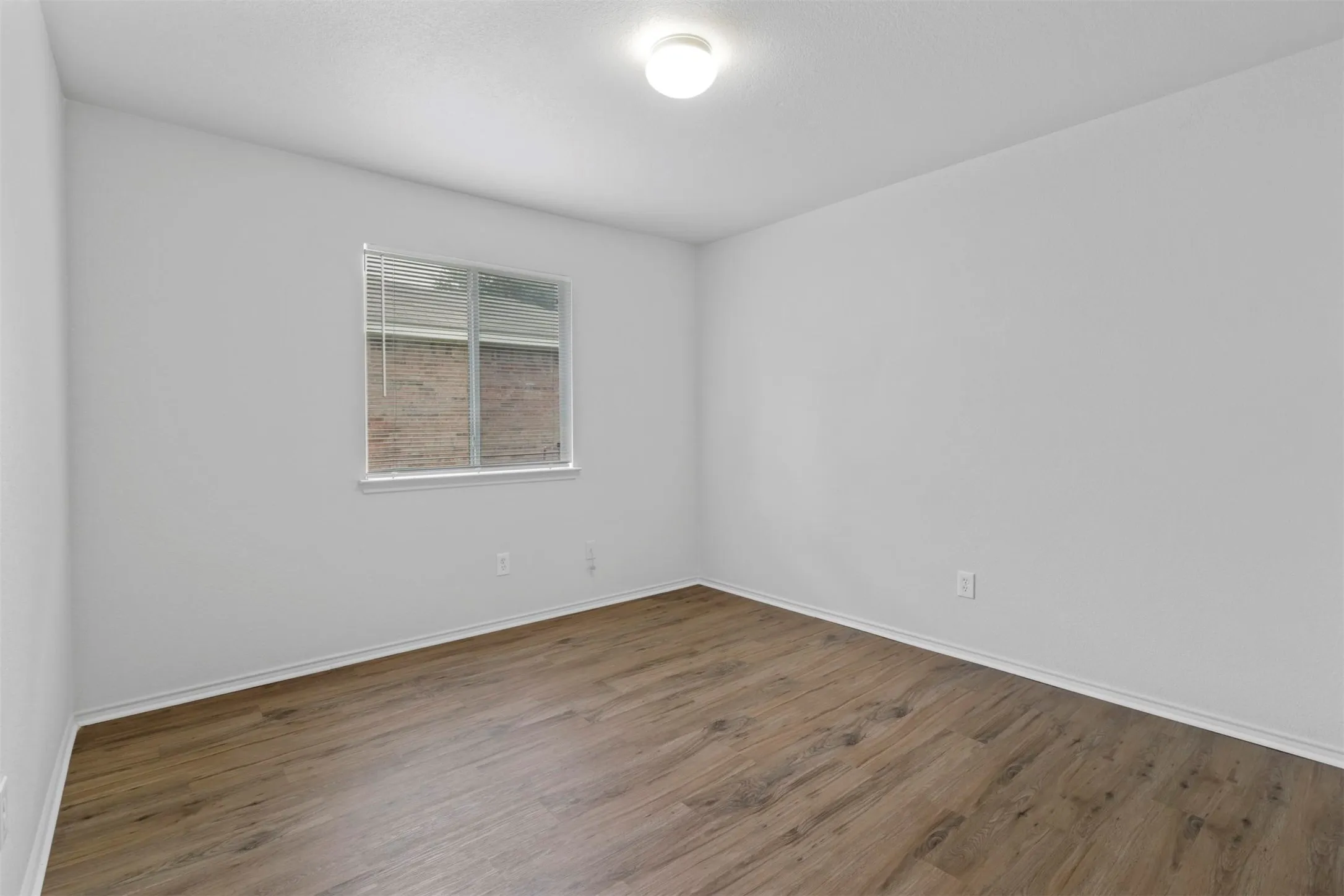 Interior room featuring wood-finish flooring, white walls, and a recessed window with blinds