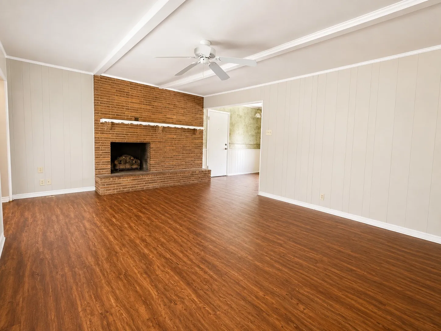 Spacious room featuring wood-finish flooring, a brick fireplace with a hearth, white vertical paneling, and a ceiling fan