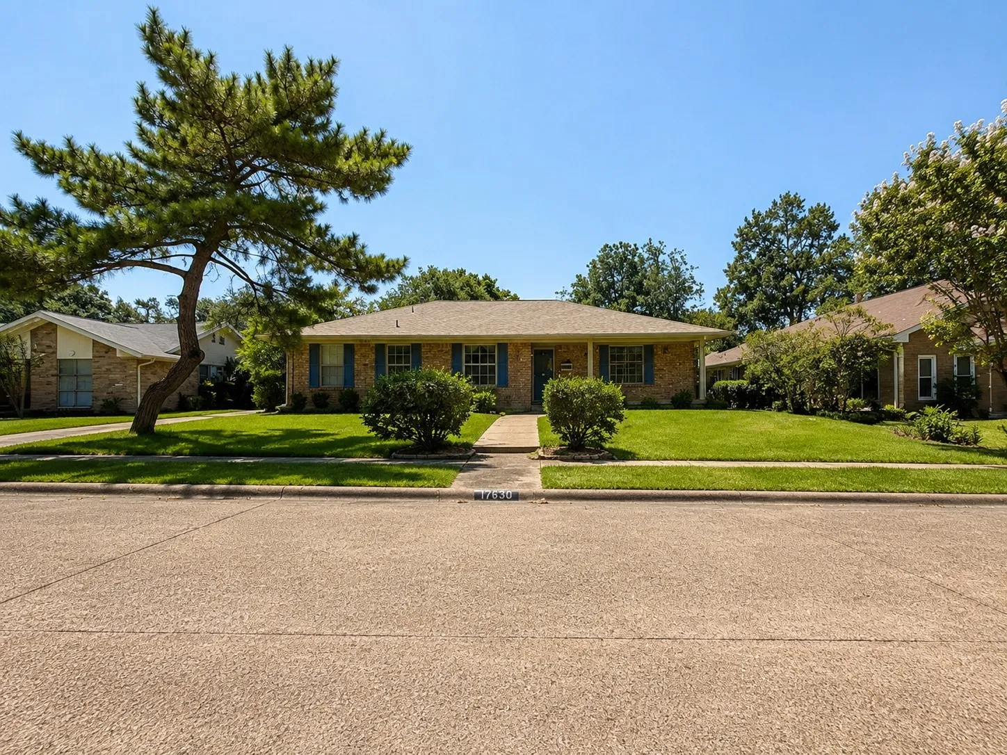 Brick exterior featuring a covered porch entry, blue louvered shutters, an established lawn, and mature landscaping