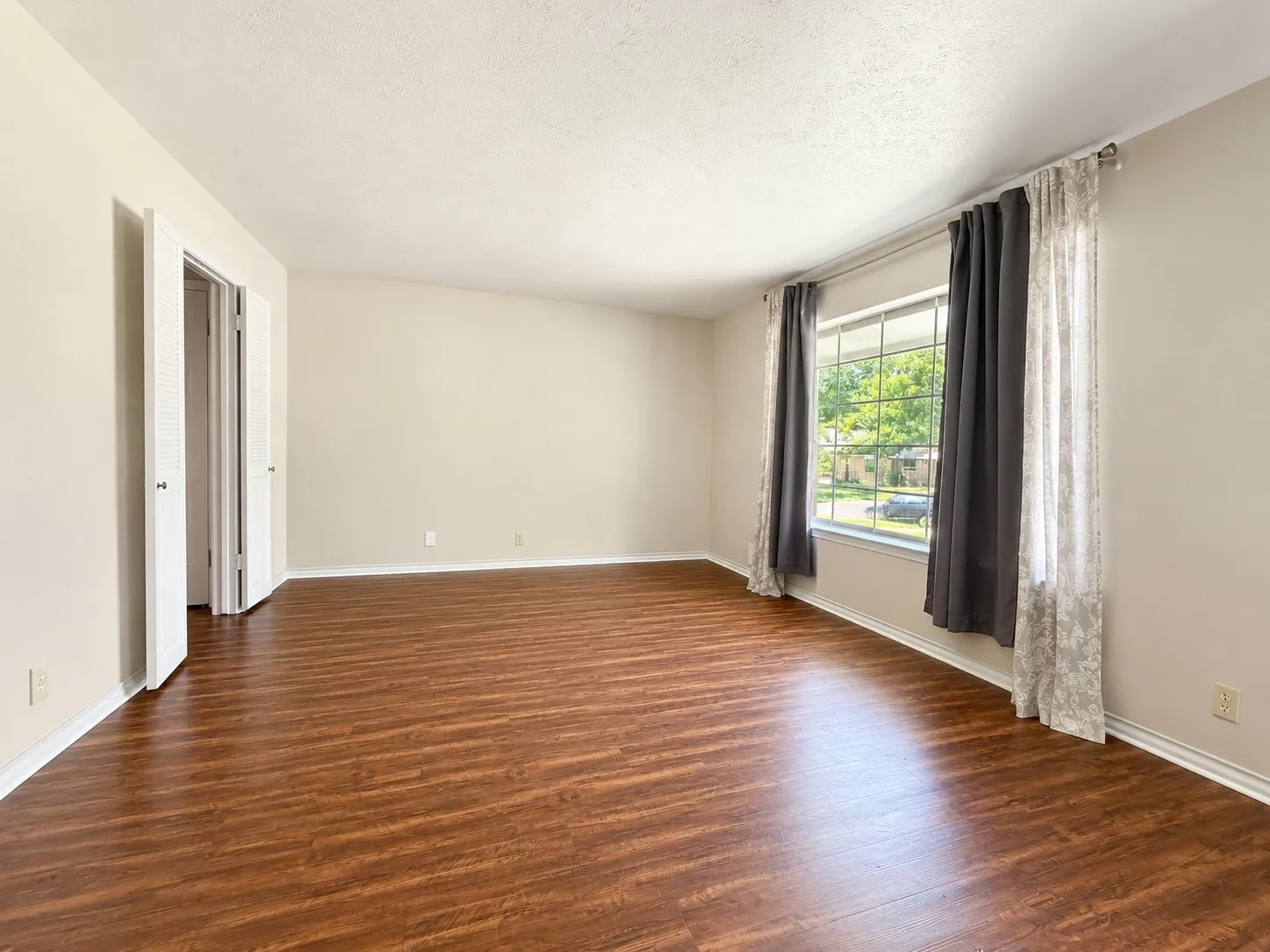 Spacious room featuring wood-finish flooring, light-colored walls, and a large window