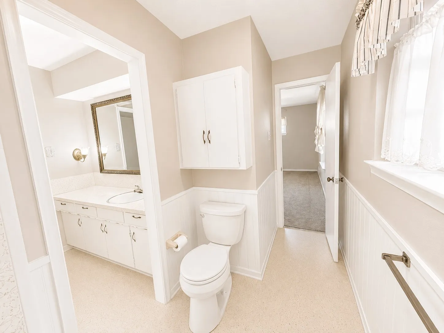 Bathroom featuring beadboard wainscoting, built-in vanity with single sink, wall-mounted cabinetry, and a toilet