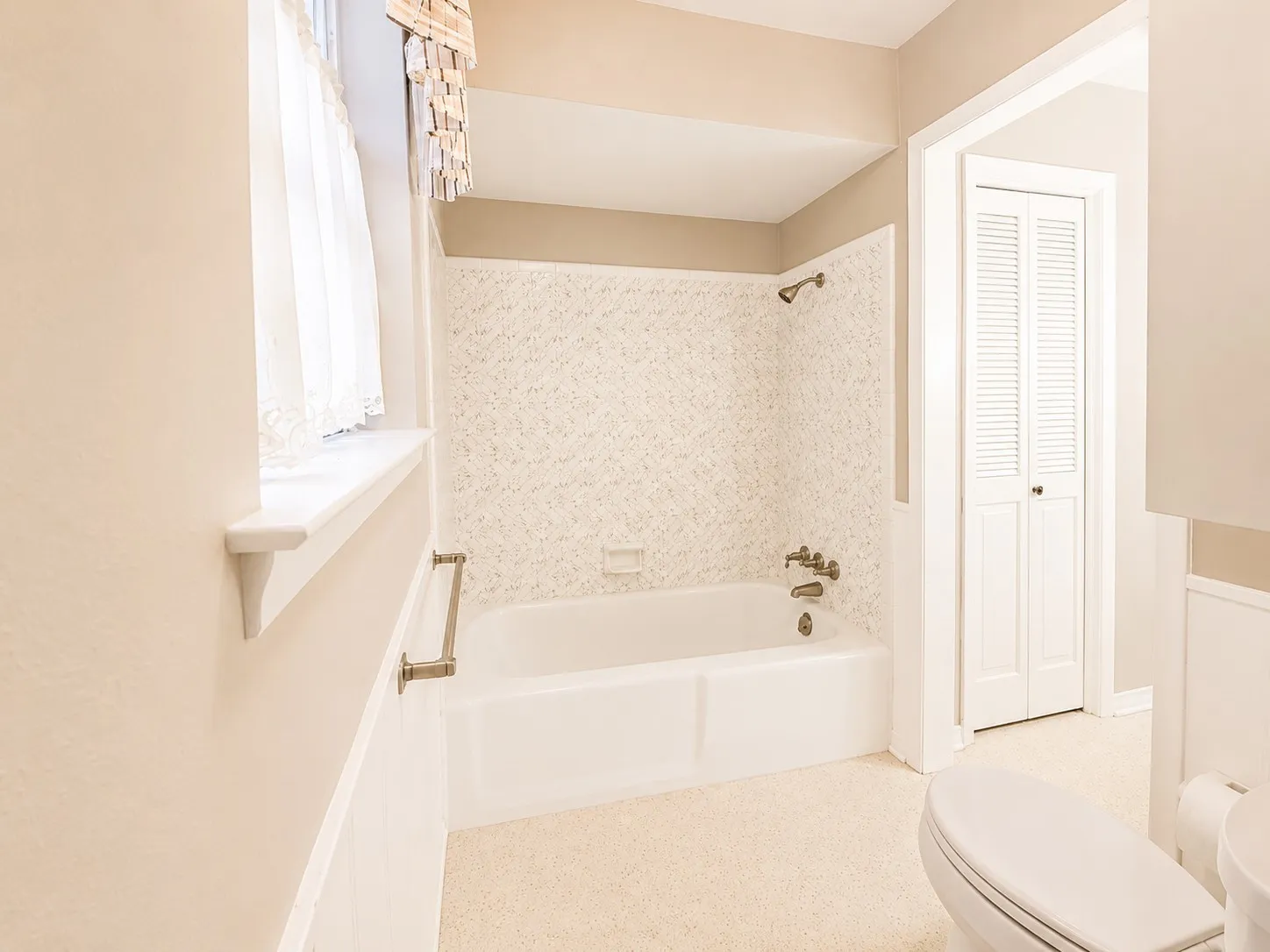 Bathroom featuring a white bathtub with tile surround, a built-in toilet, and a louvered bi-fold door