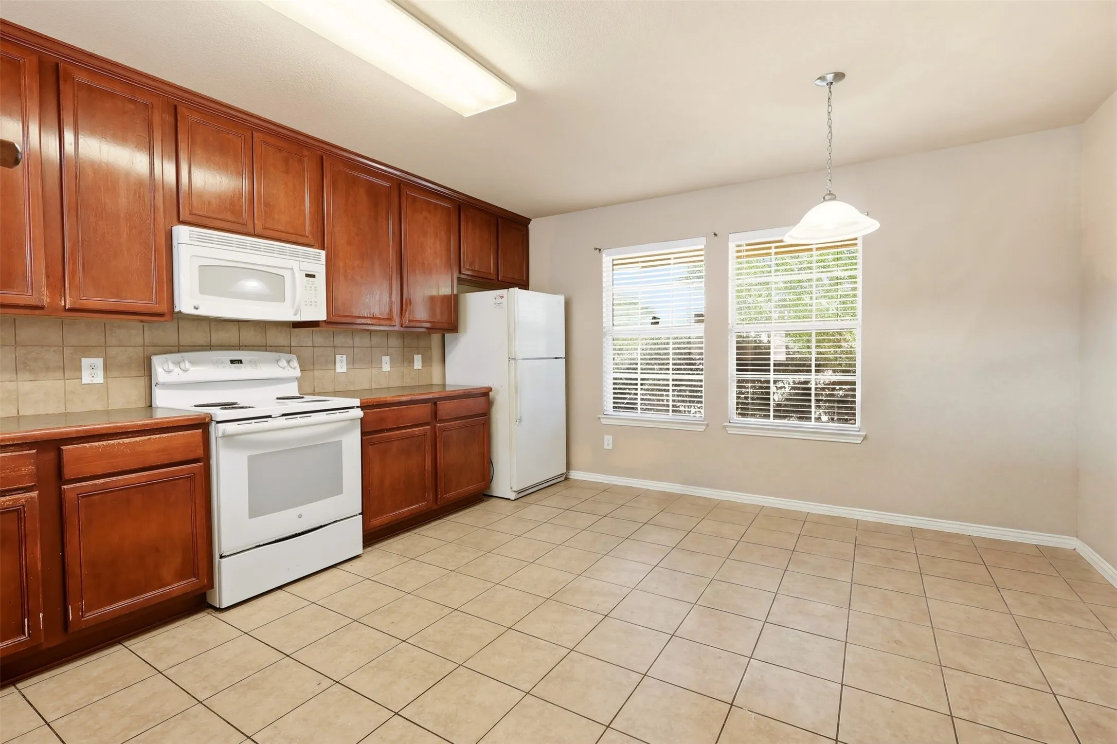 Kitchen and dining area featuring wood cabinetry, tile flooring, and integrated white appliances