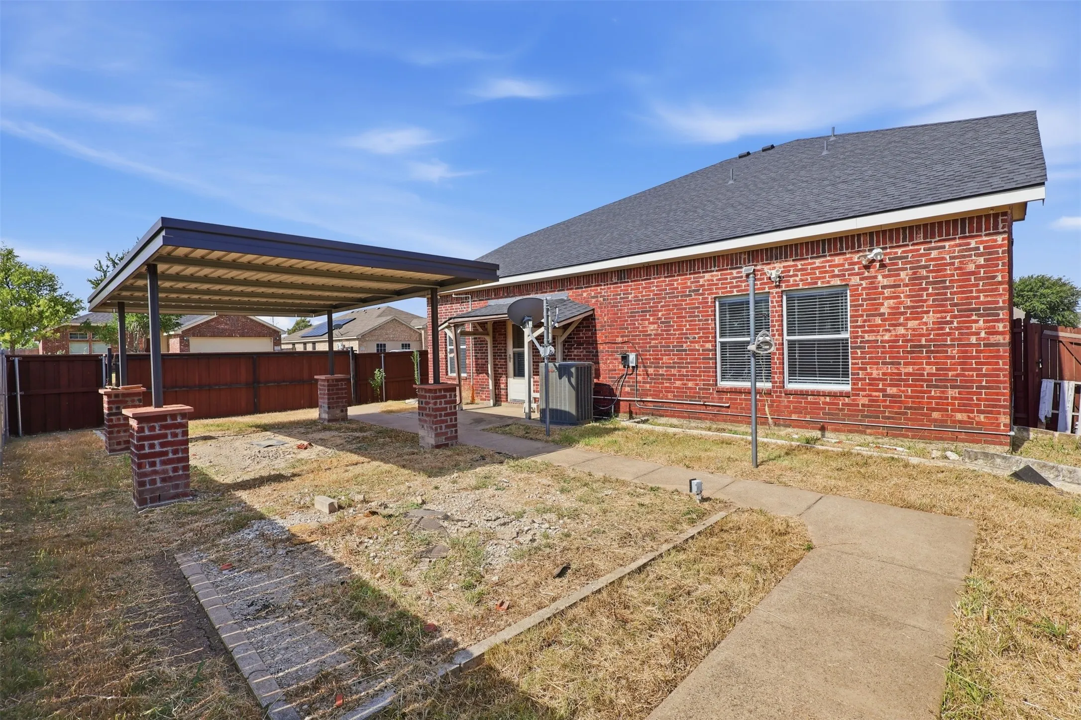 Brick exterior home showcasing a spacious backyard with concrete patio, mature landscaping, and covered pergola structure