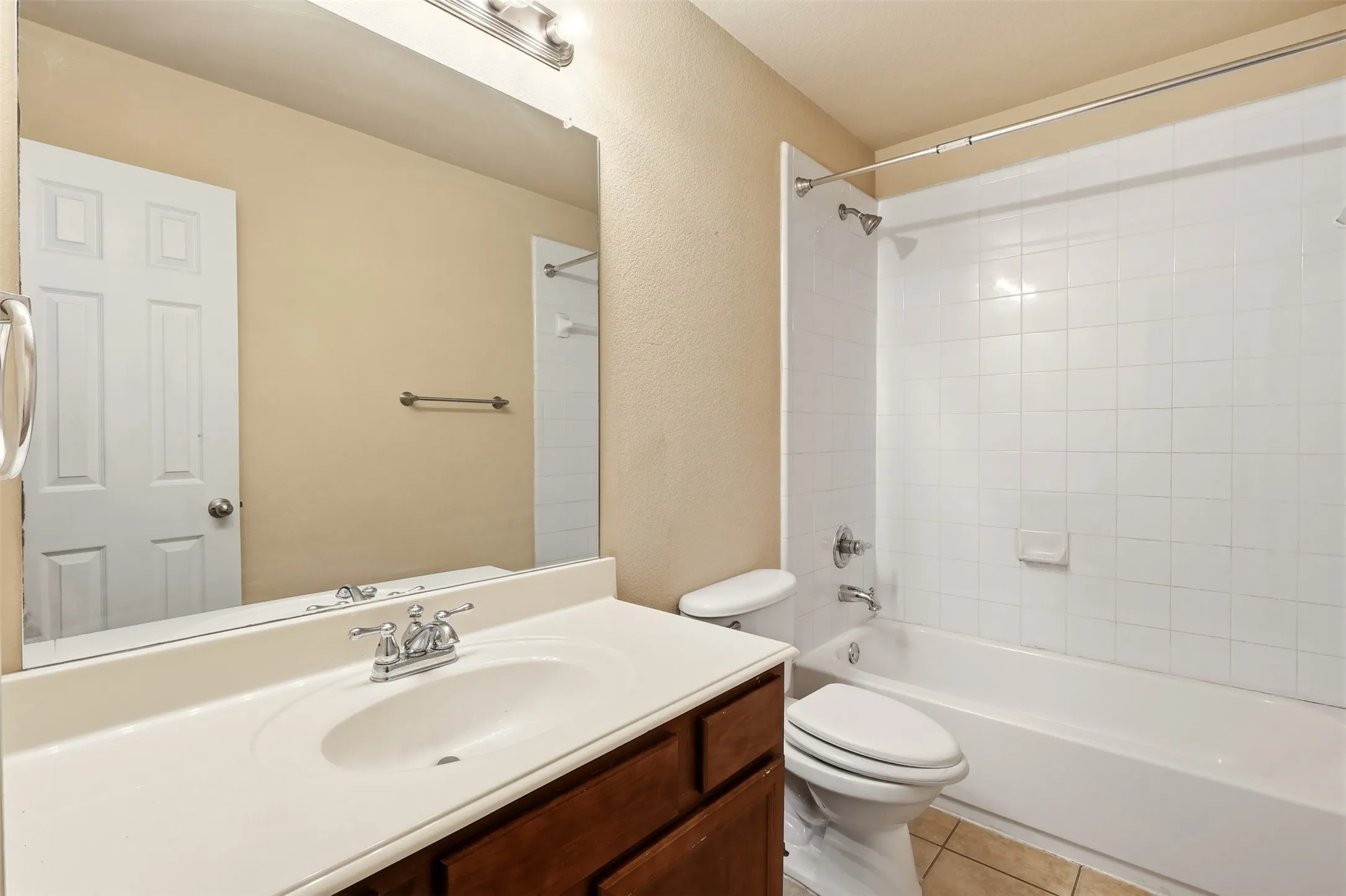 Bathroom featuring a white vanity with integrated sink, chrome faucet, wood-finish cabinetry, and a white tiled shower-over-tub combination