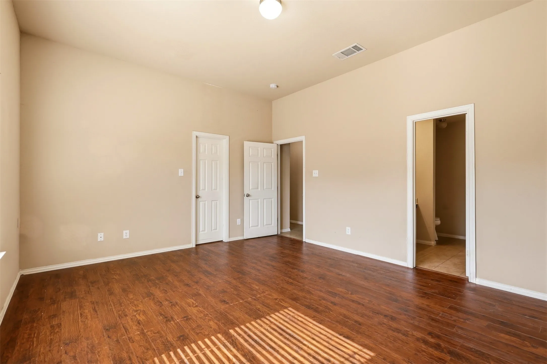 Spacious interior room featuring wood-finish flooring, a neutral color palette, multiple entryways, and a vaulted ceiling