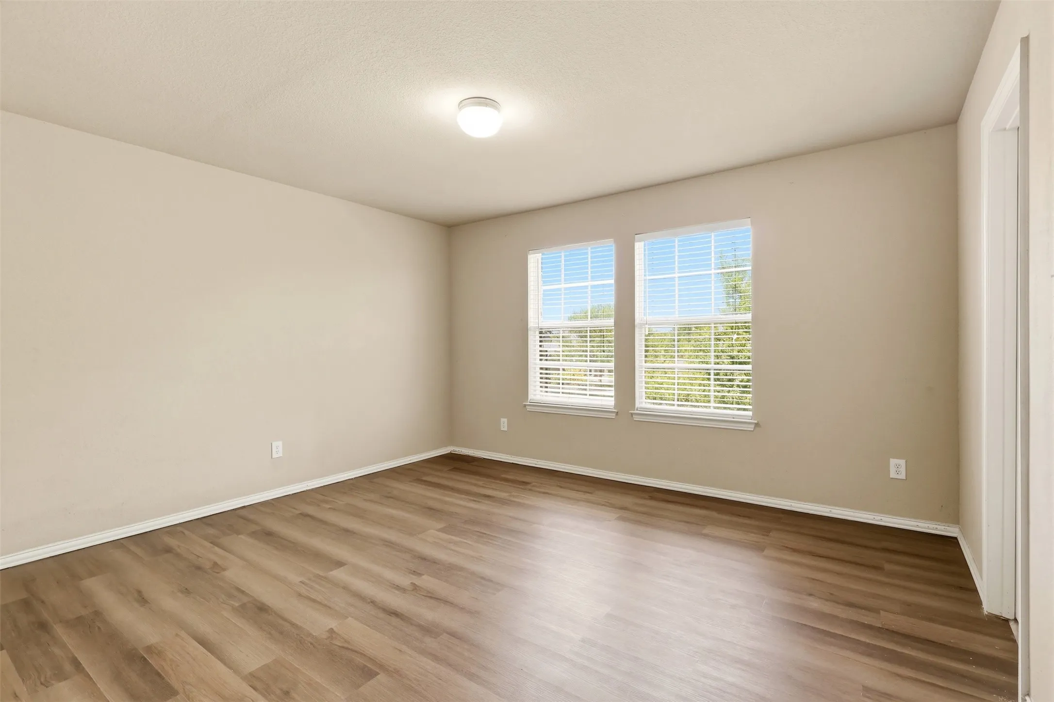 Room featuring wood-finish flooring, neutral wall tones, and two windows with​​‌​​​​‌​​‌‌​‌‌​​​‌‌​‌​‌​‌​​​‌​​ blinds