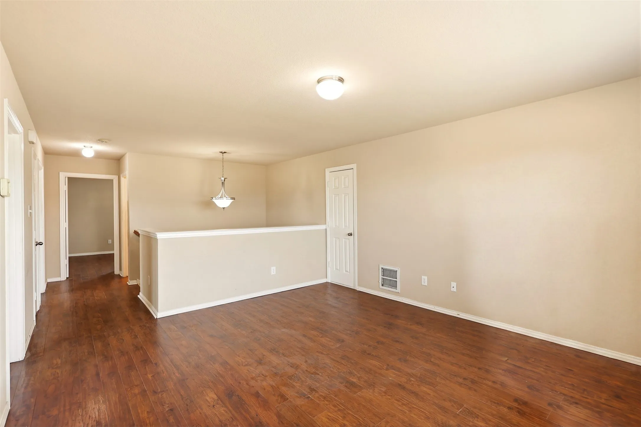 Spacious open-concept living area featuring rich wood-finish flooring throughout, neutral wall finishes, and wainscoting detail