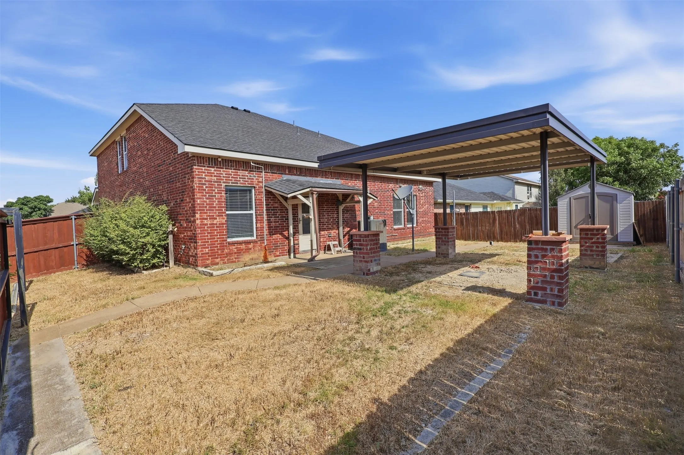 Rear exterior featuring a brick facade, covered patio with brick pillars, a detached storage shed, and a wooden privacy fence