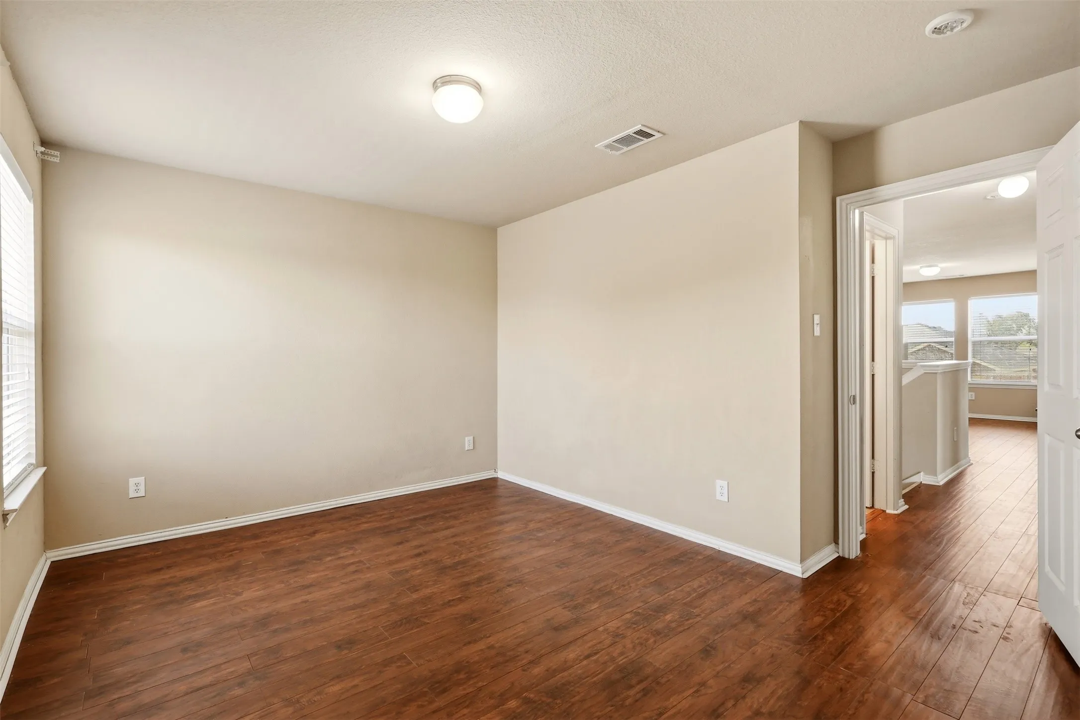 Spacious room featuring wood-finish flooring, neutral-toned walls, a window with blinds, and a flush mount ceiling light