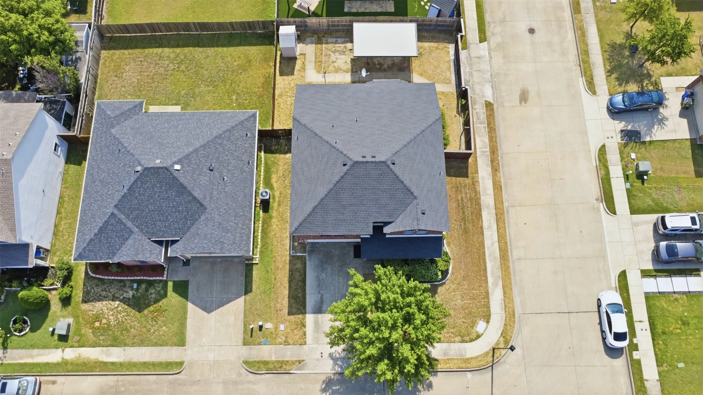 Aerial view showcasing a residential property with a dark shingle roof and an attached concrete driveway
