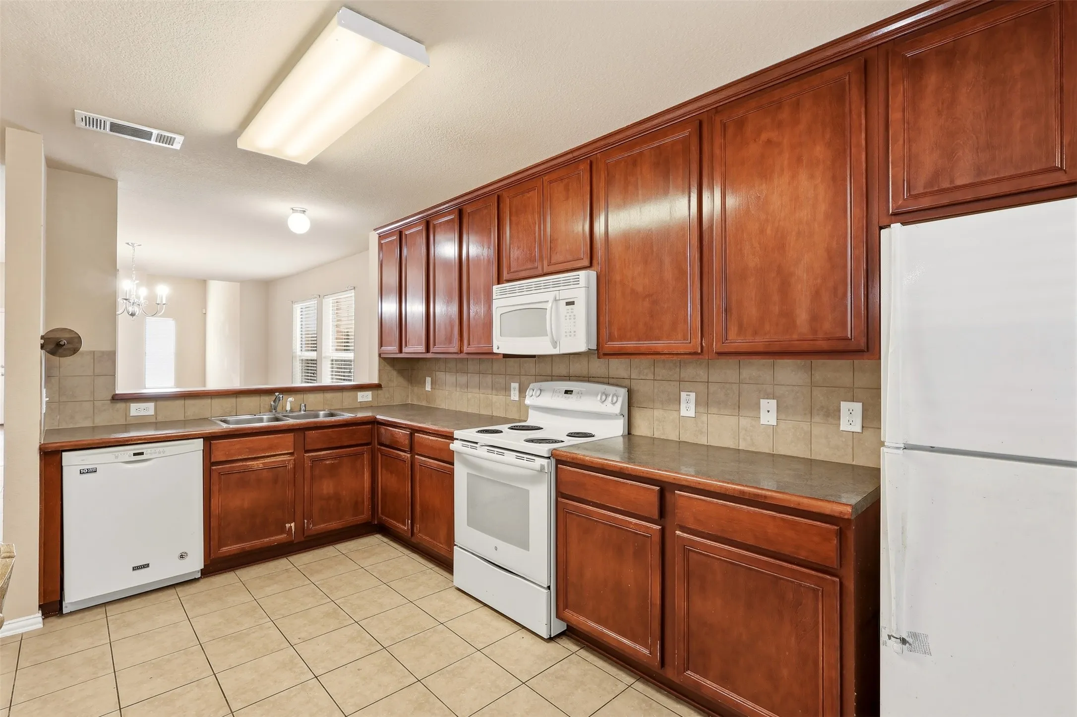 Kitchen featuring extensive wood cabinetry, tile flooring, white appliances, and a pass-through window to an additional room