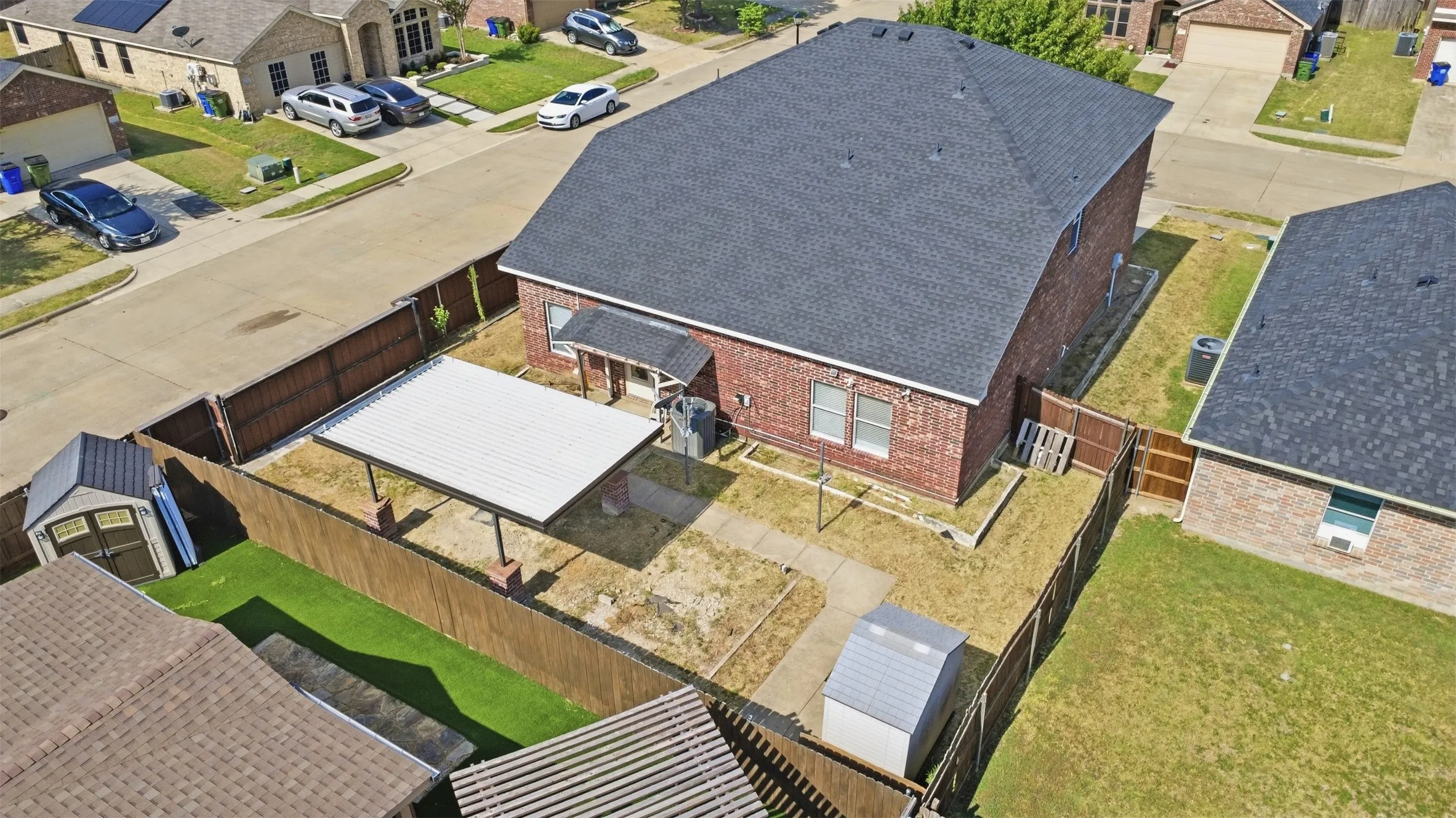 Brick exterior residence featuring a dark shingle roof, a covered patio structure, and a concrete pathway leading to the rear entrance