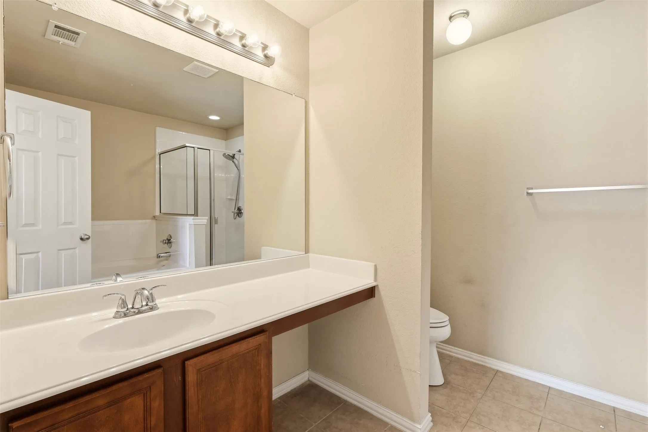 Bathroom featuring a single-basin vanity with a white countertop and wood-finish cabinetry, a large wall-mounted mirror, and tile flooring