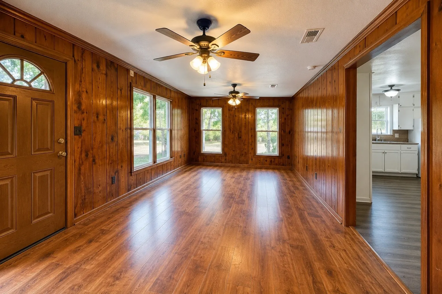 Wood-finish flooring throughout, wood paneling, multiple windows, and two ceiling fans with integrated lighting