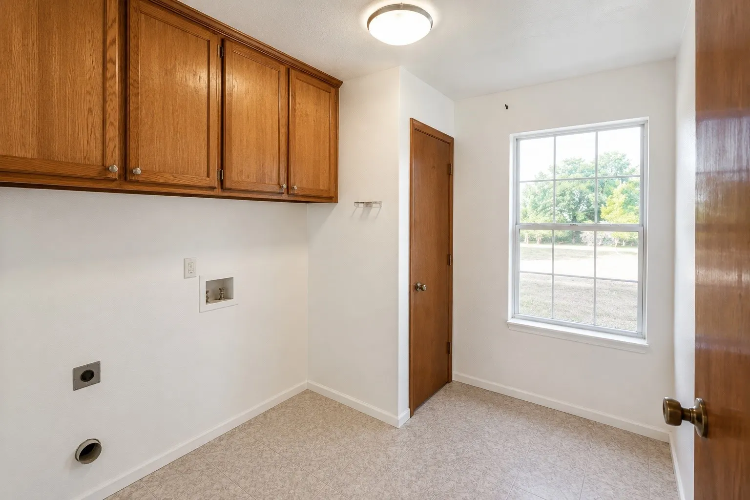Overhead cabinetry, white walls, light-colored flooring, window with natural light, and a solid door