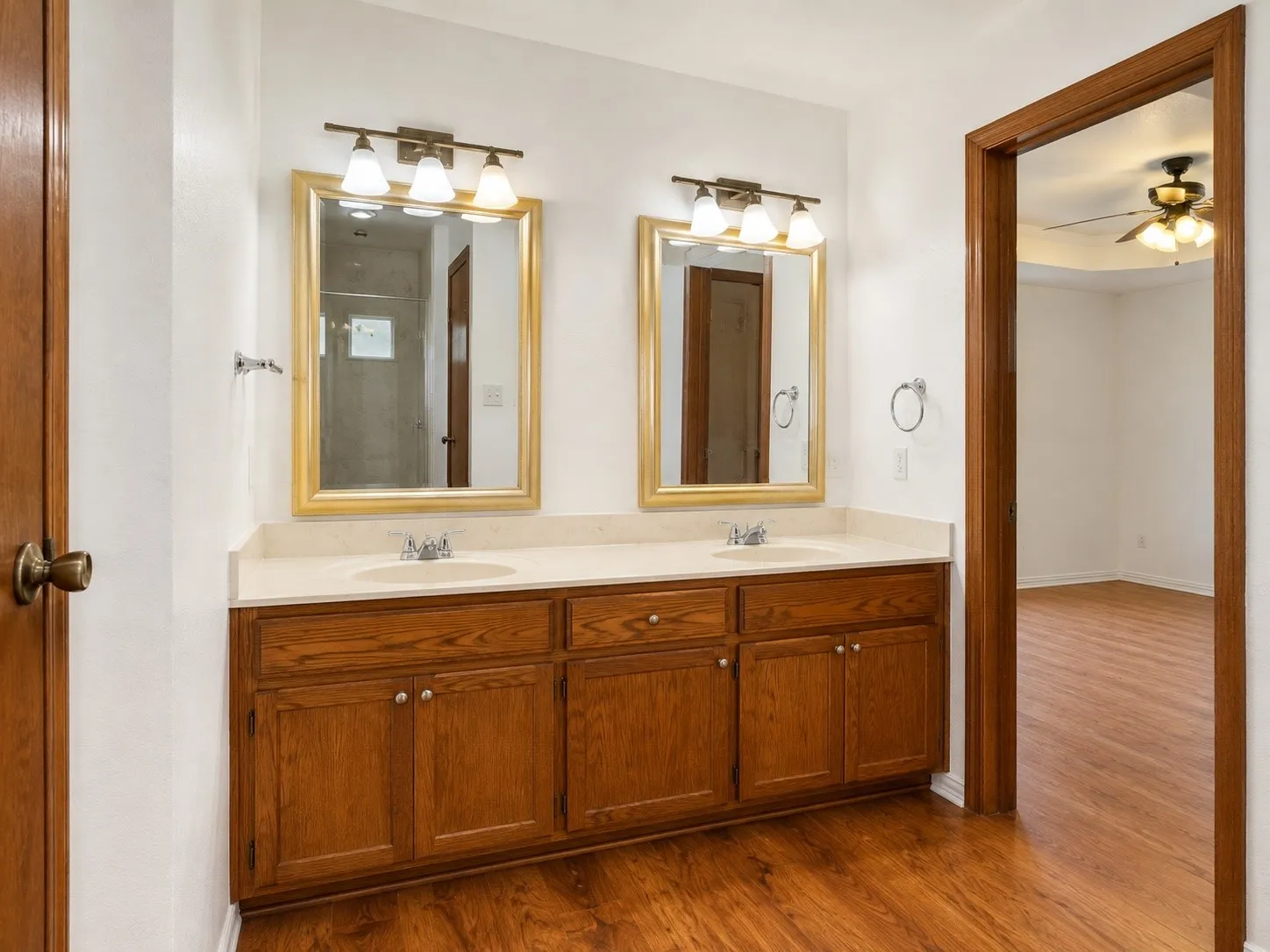 Dual-sink vanity with wood cabinetry, framed mirrors with integrated lighting, and wood-finish flooring