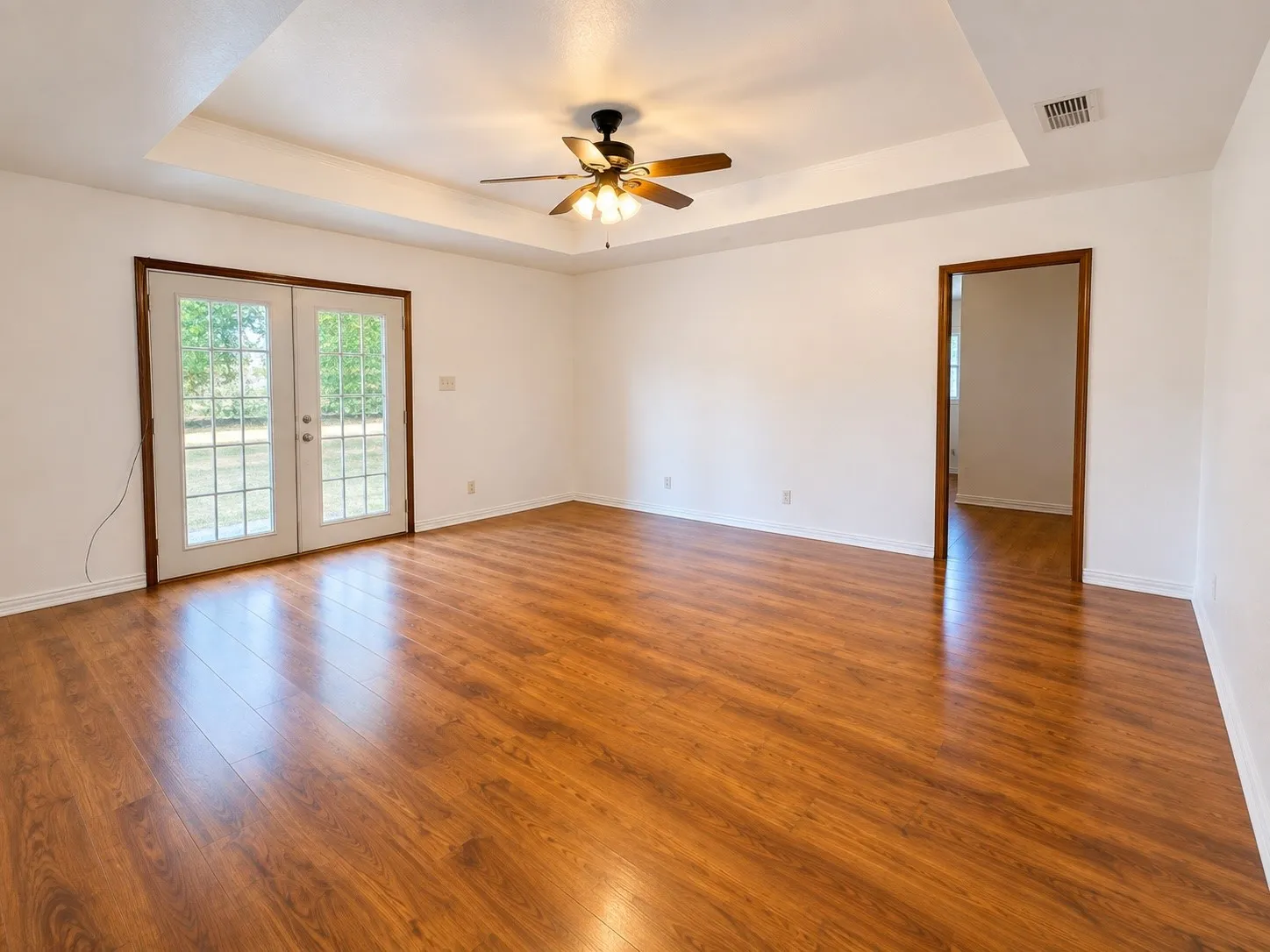 Wood-finish flooring throughout, tray ceiling, ceiling fan with integrated lighting, and French doors