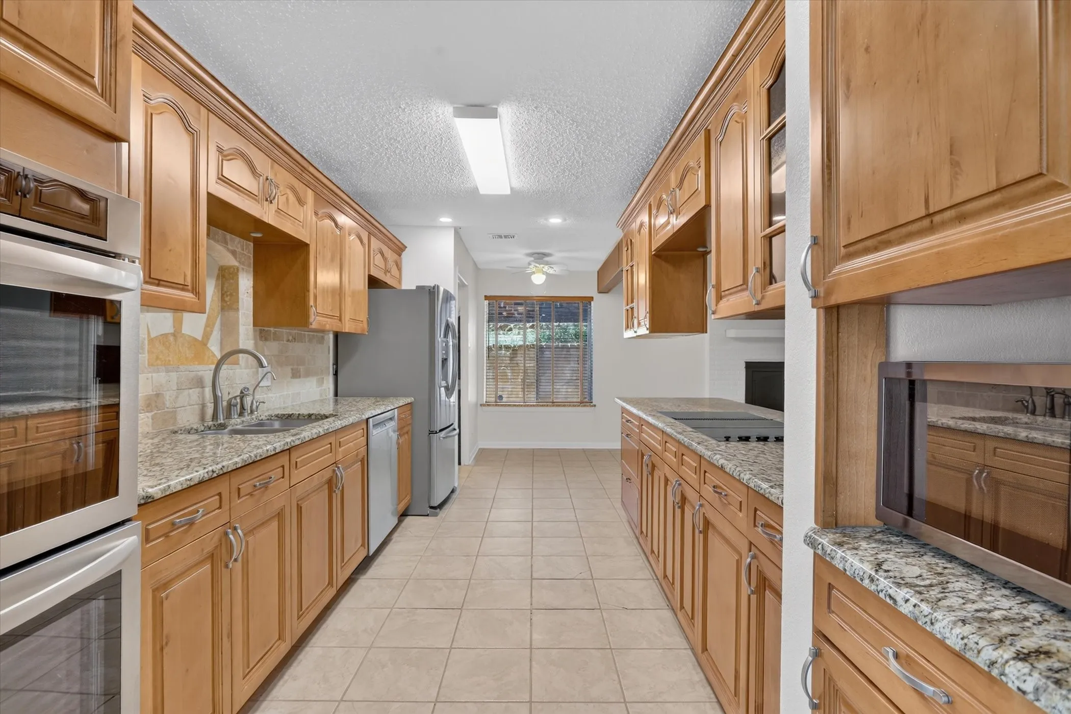 Kitchen featuring light wood cabinetry, granite-style countertops, stainless steel appliances, and a tile backsplash
