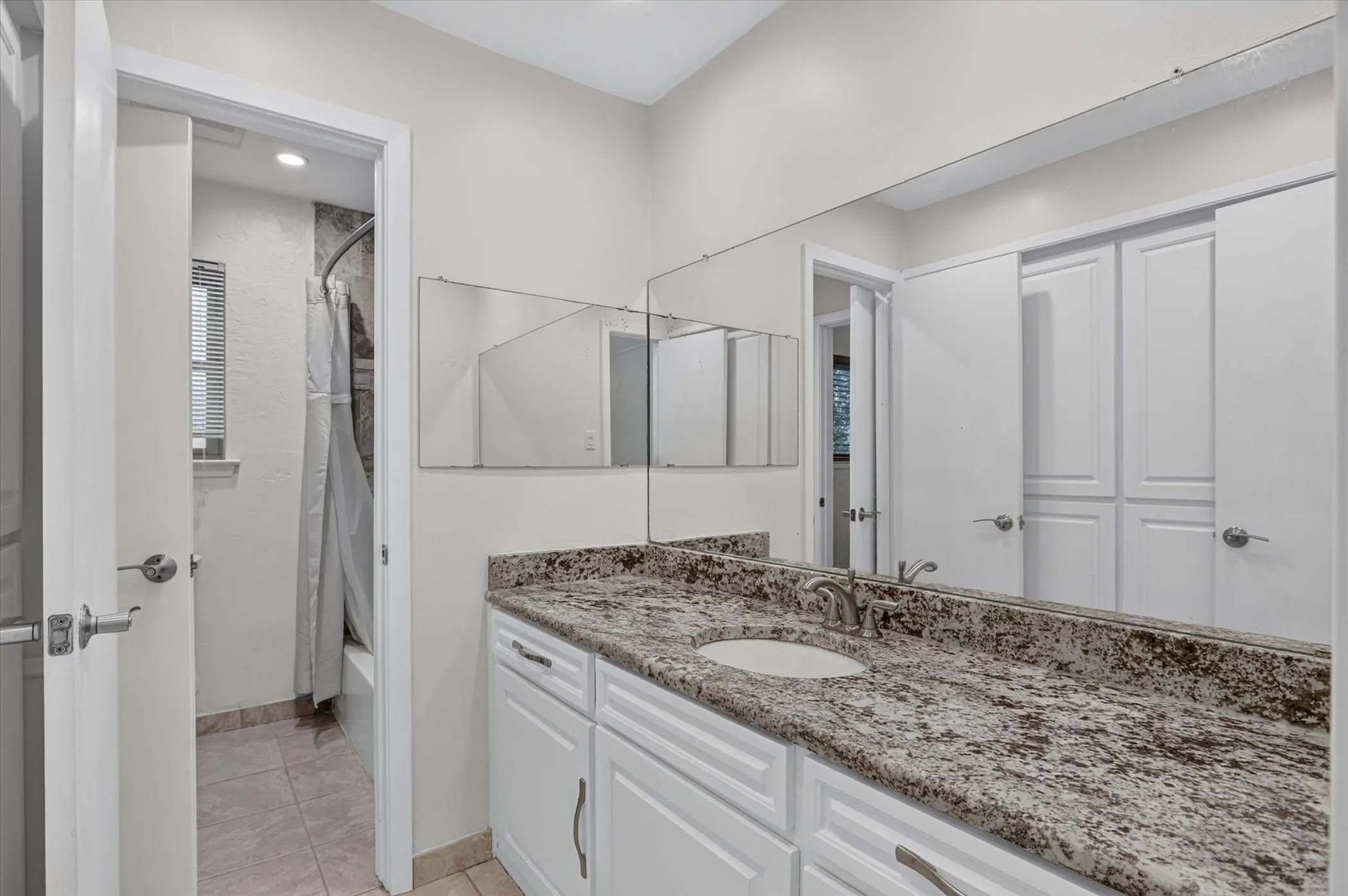 Vanity with integrated sink, patterned countertop, white cabinetry, and full-width mirror