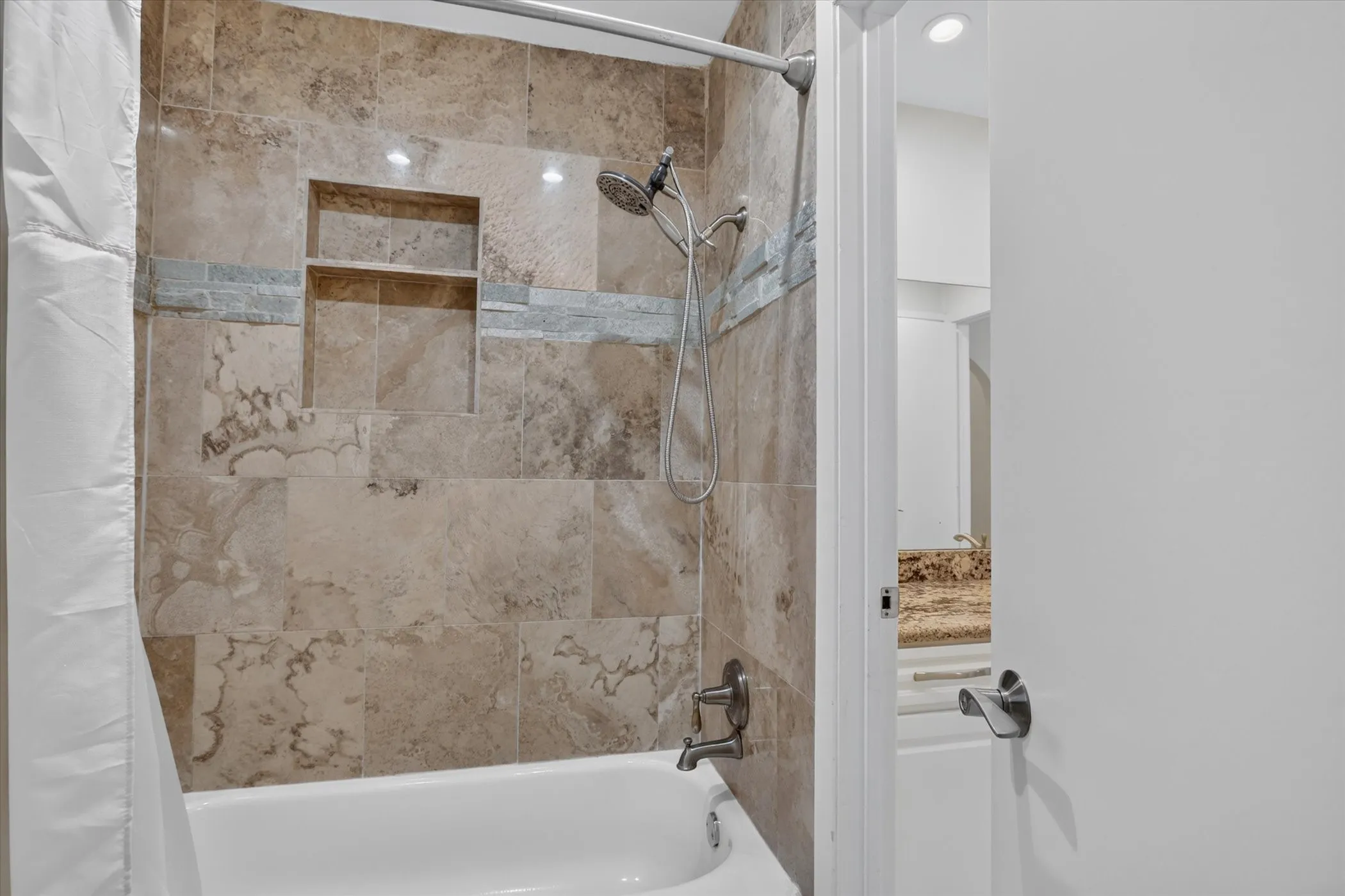 Bathtub with a tiled surround featuring an integrated niche, brushed nickel showerhead, and coordinating hardware