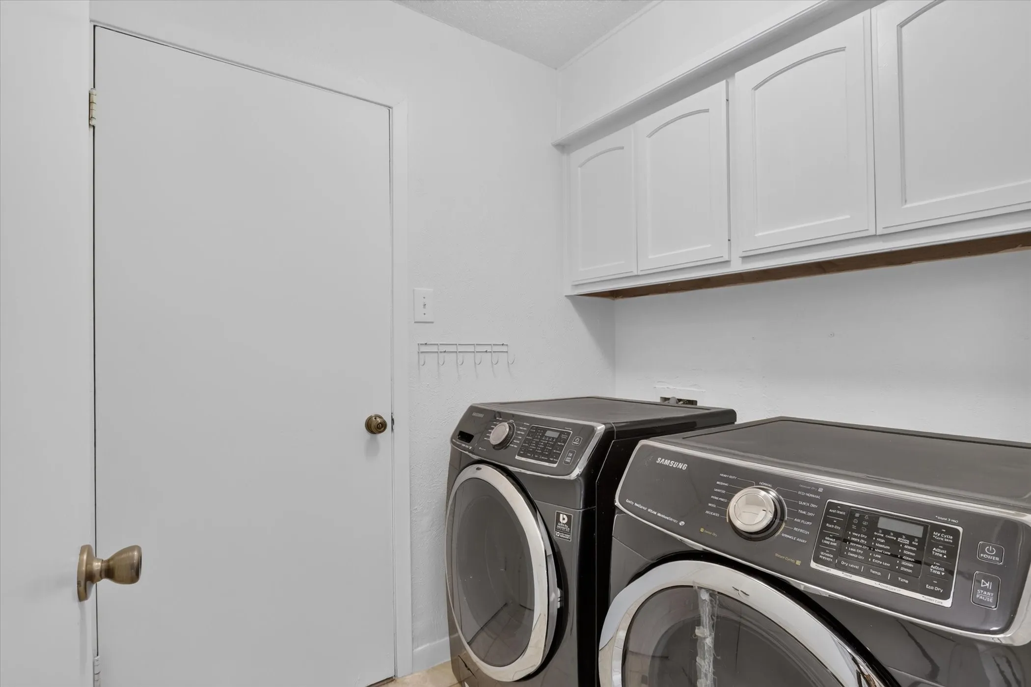 Laundry area featuring upper cabinetry with arched panel doors and a light neutral color palette