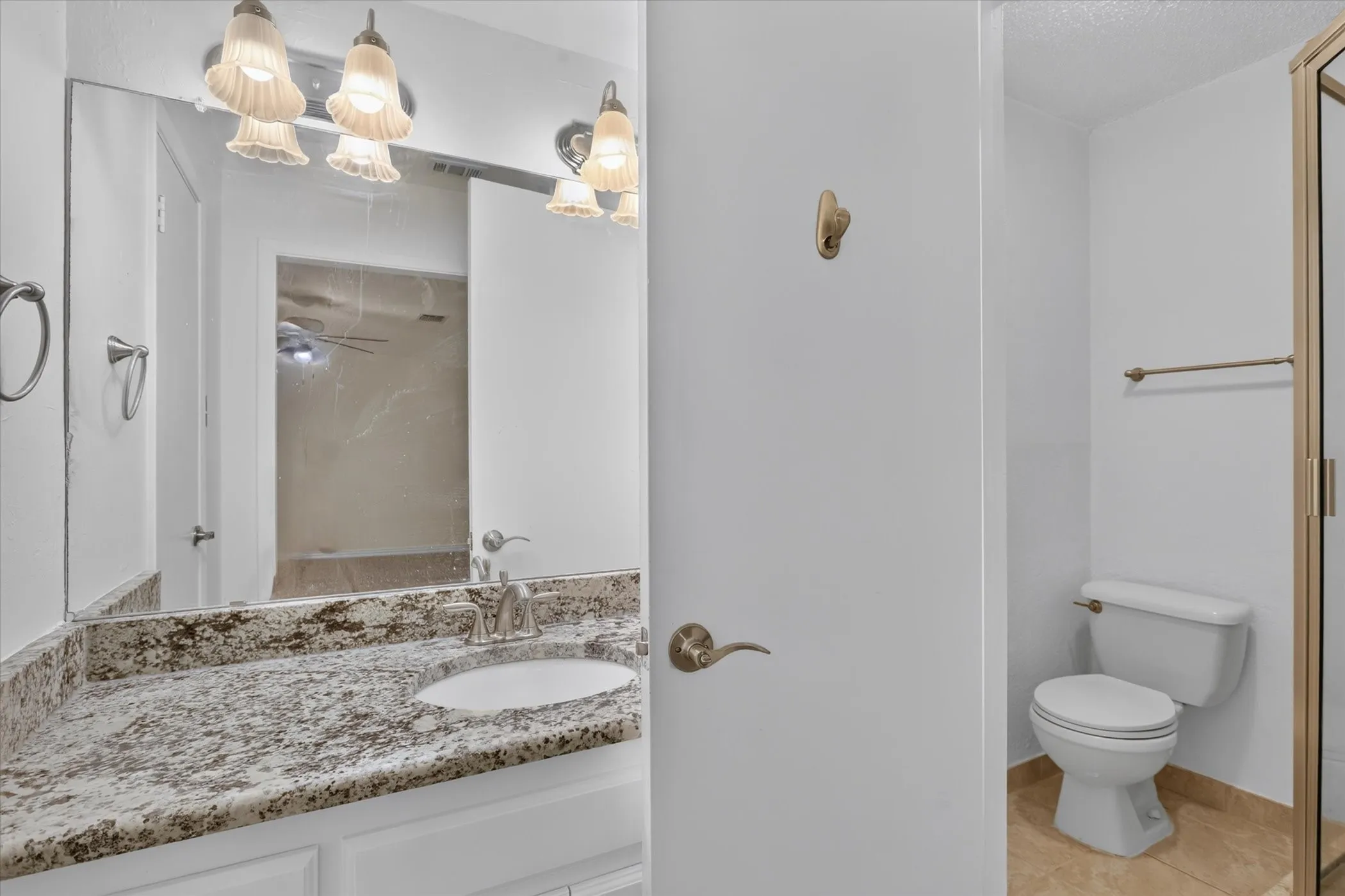 Master bathroom featuring dual vanity with speckled stone countertop, recessed mirror with integrated lighting, separate water closet, and cork-finish flooring