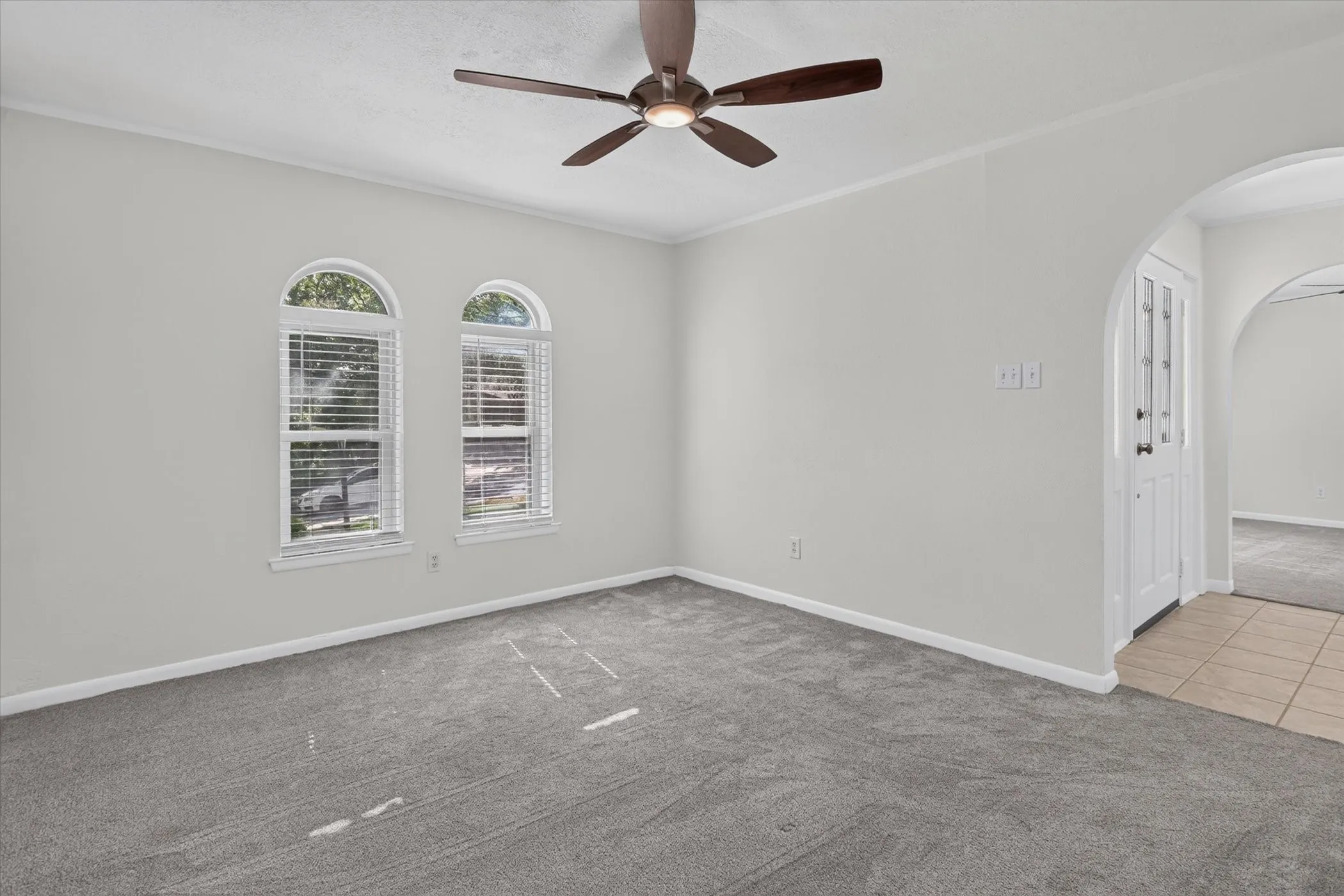 Arched windows with blinds, gray carpeting, neutral wall paint, and a ceiling fan with integrated lighting