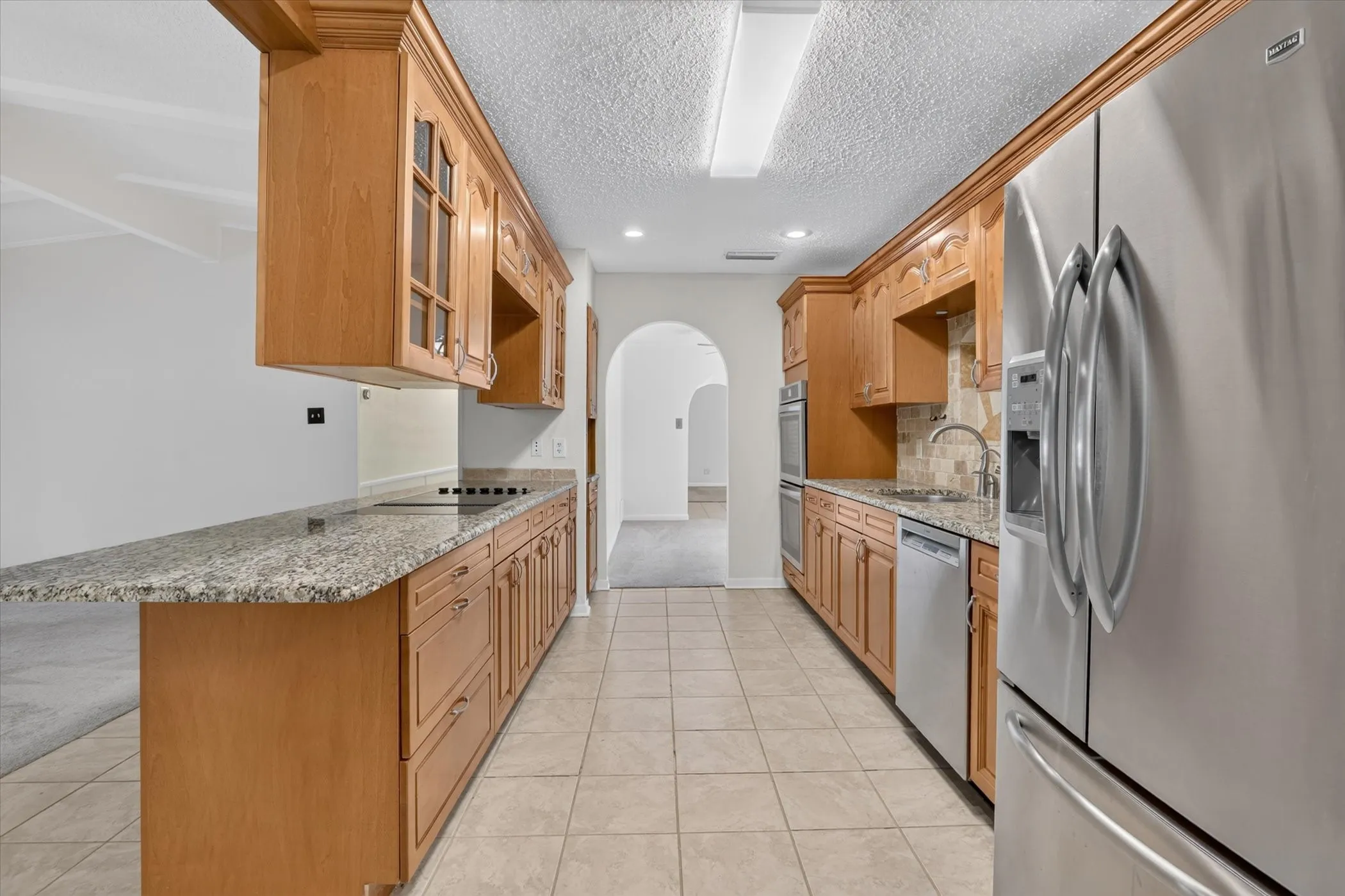 Galley kitchen featuring wood cabinetry, granite countertops, stainless steel appliances, and tile flooring