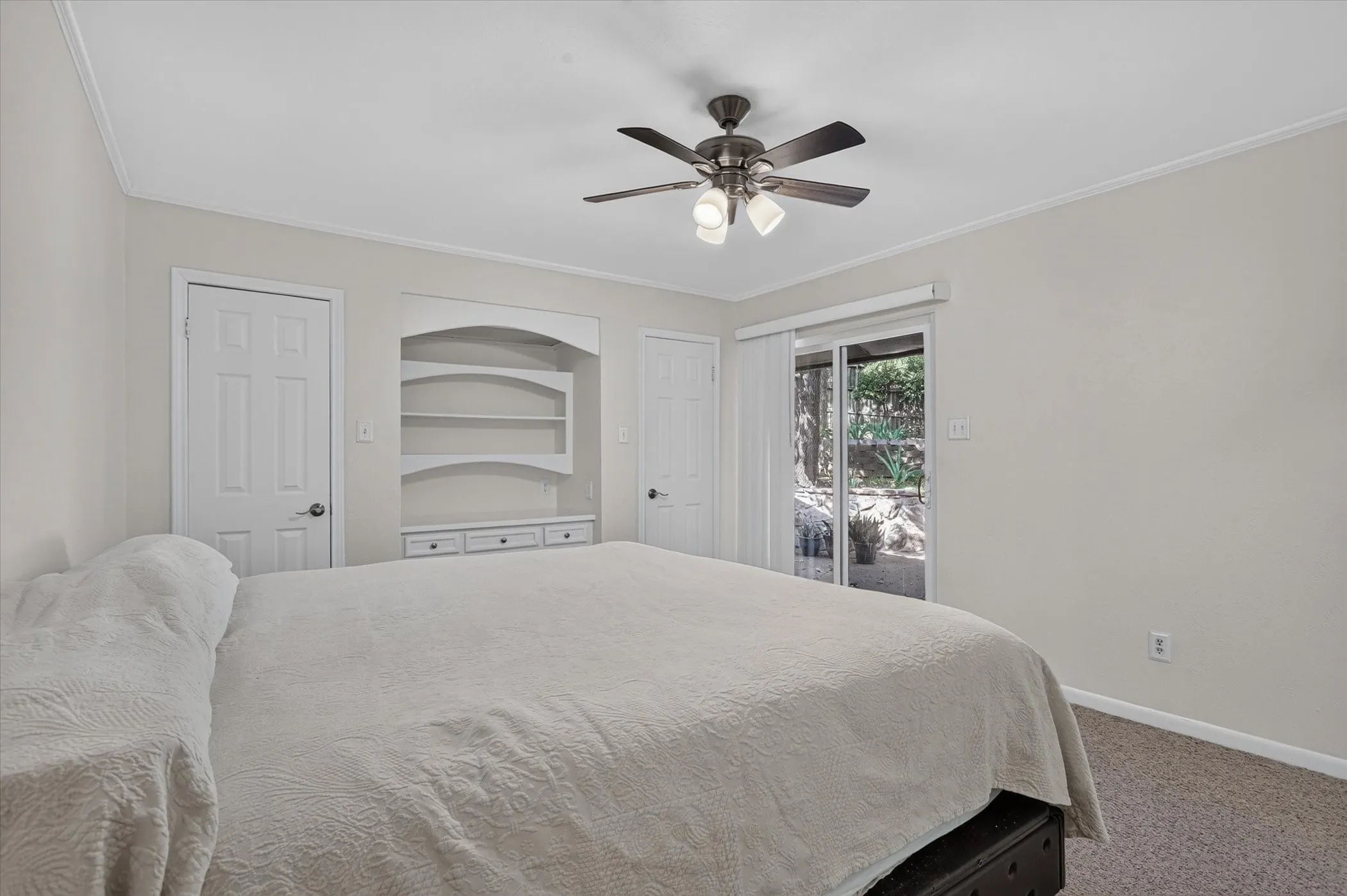 Built-in shelving unit with drawers, ceiling fan with integrated lighting, two panel interior doors, and sliding glass door