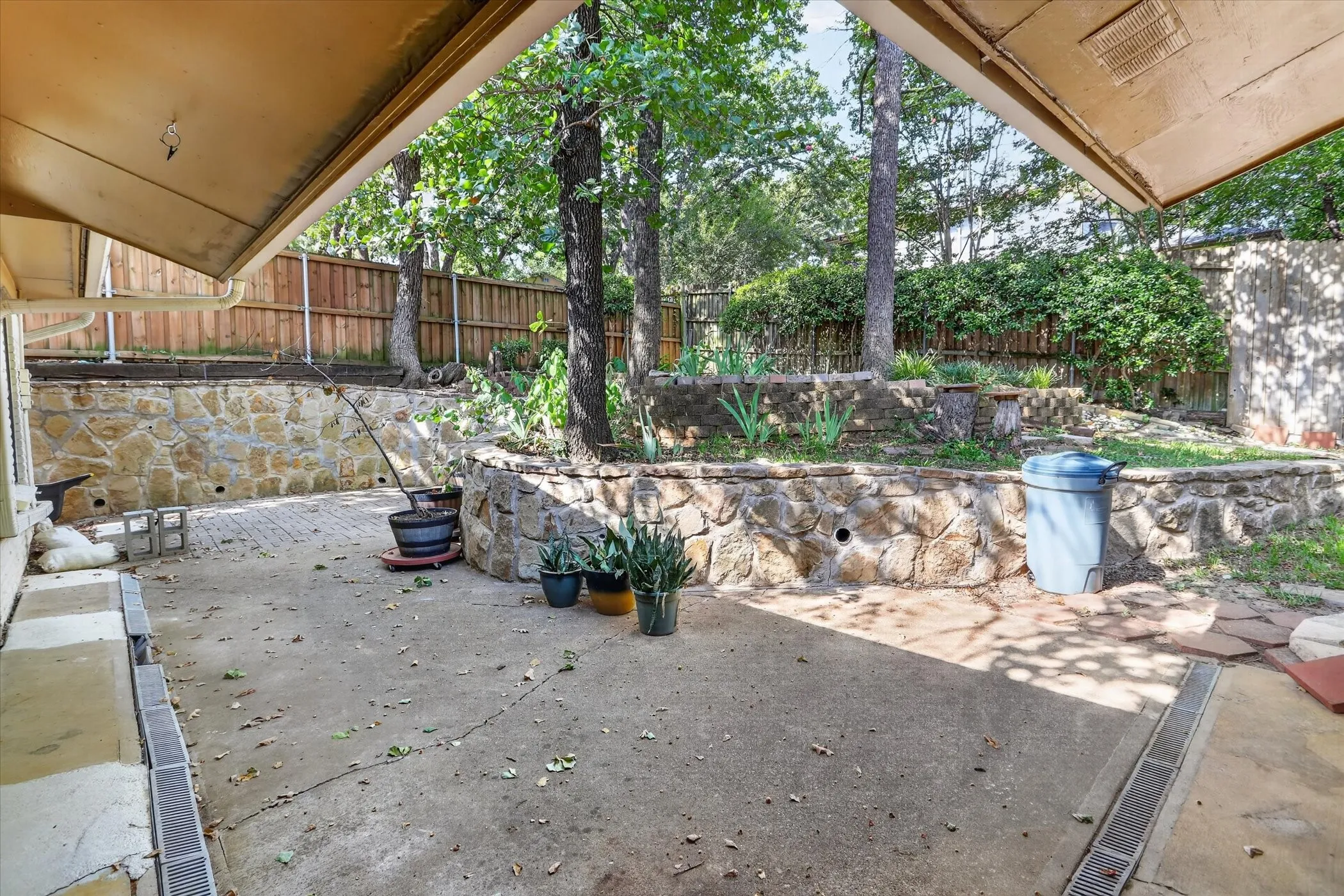 Concrete patio with integrated drainage, stone retaining walls, and mature trees