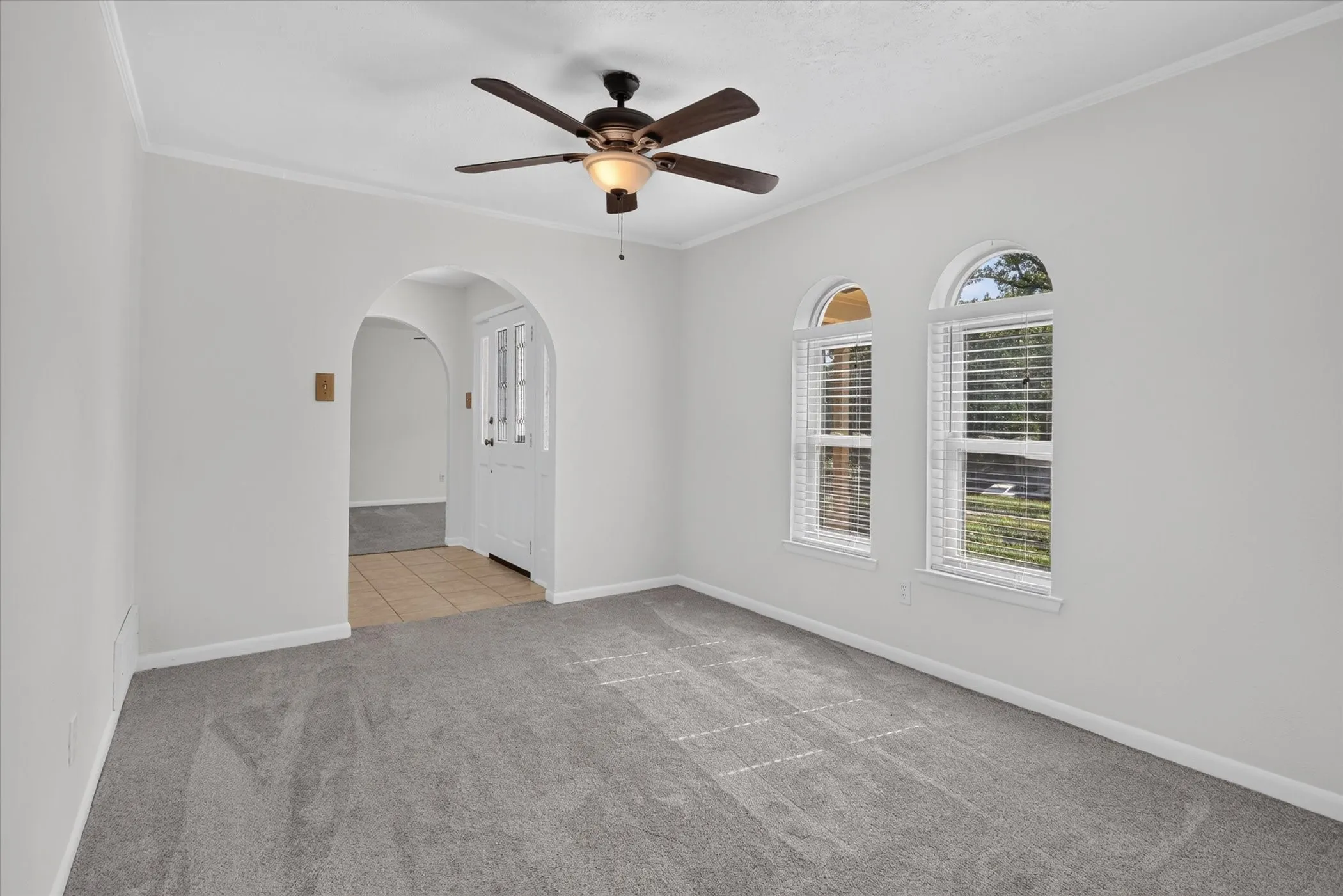 Arched entryway, two arched windows, installed window blinds, ceiling fan with integrated lighting, and carpet flooring