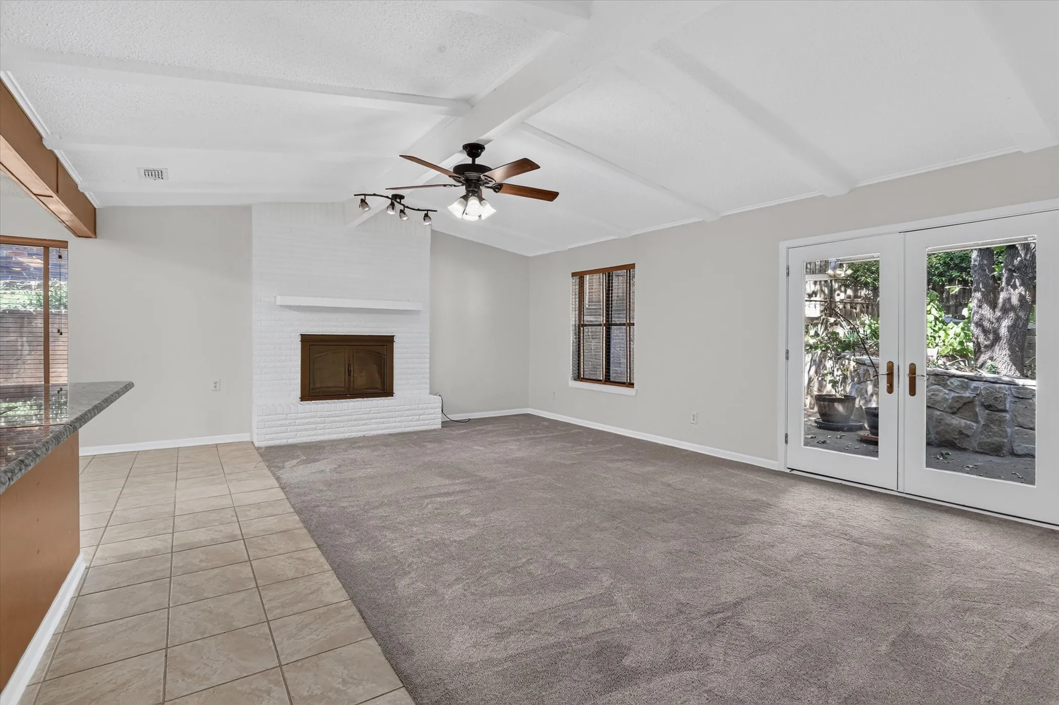 Spacious open-concept living area featuring vaulted ceilings, a ceiling fan with integrated lighting, tile flooring, and a fireplace with white surround and wood-finish mantel