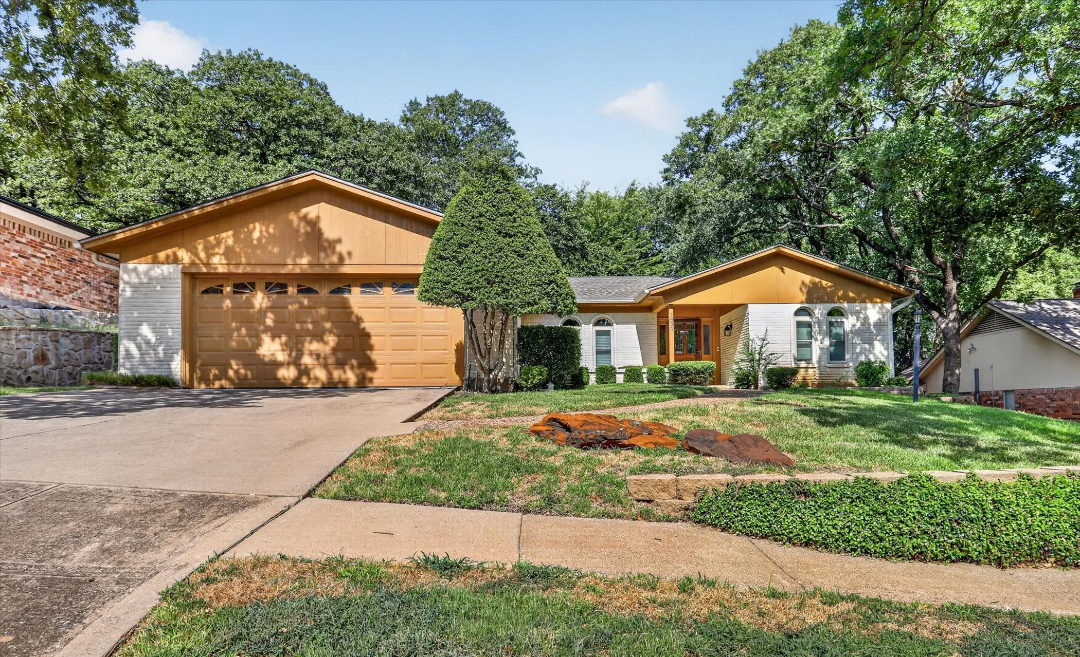 White brick exterior with wood-finish siding, arched windows, and an integrated two-car garage