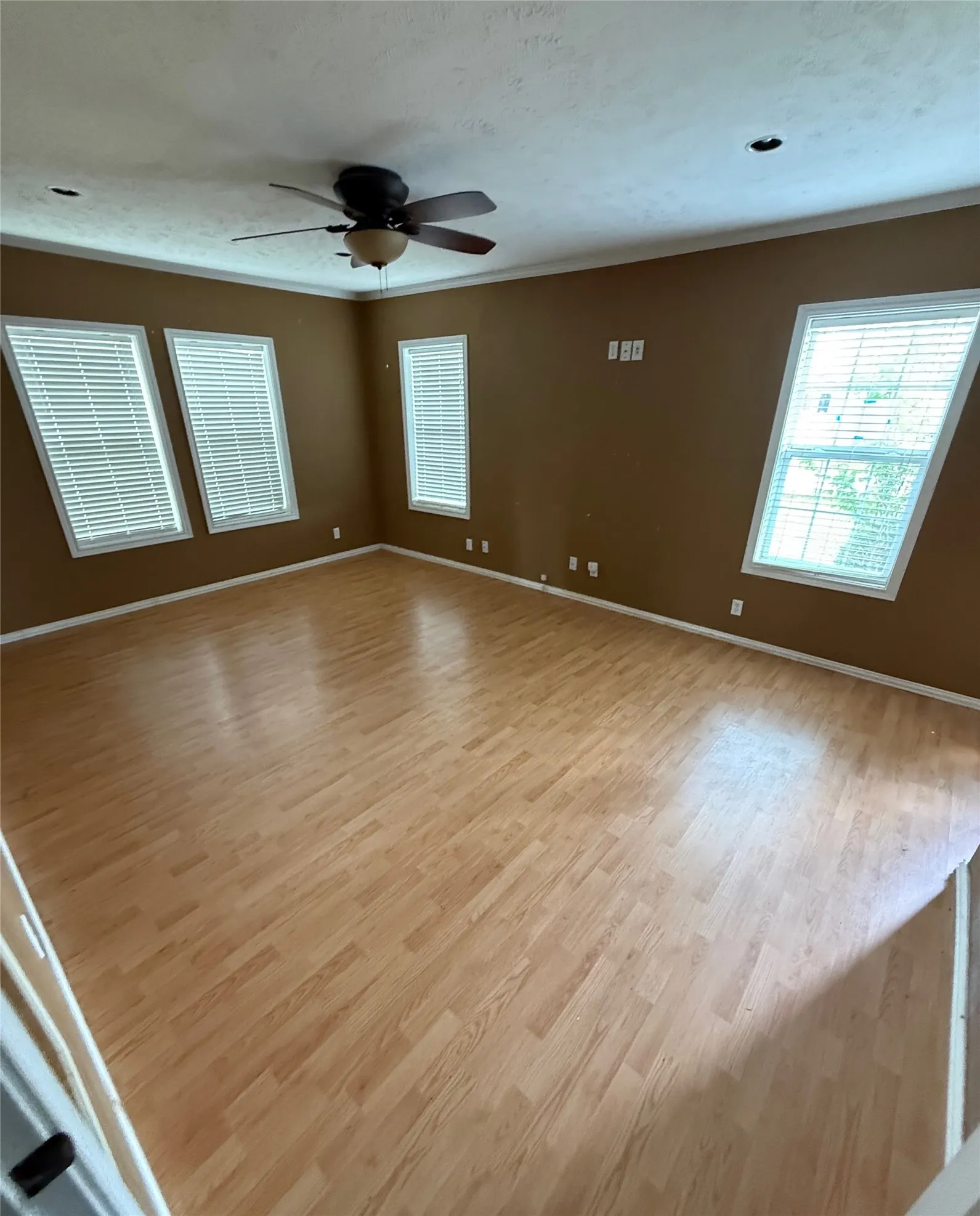 Spacious interior room featuring wood-finish flooring, a ceiling fan with light fixture, and multiple windows with blinds