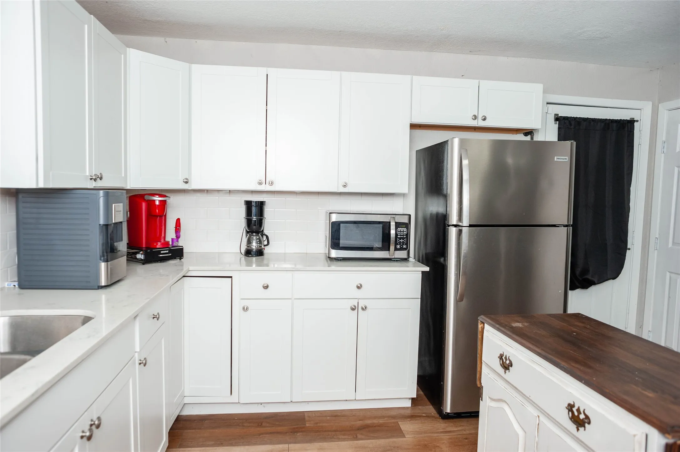 White shaker-style cabinetry, stainless steel sink, light-colored countertops, white subway tile backsplash, and wood-finish flooring